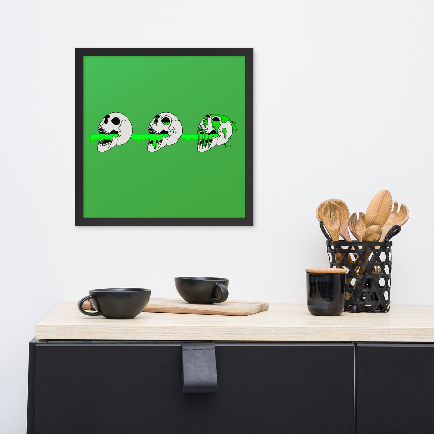Framed artwork of a 16x16 framed poster of 3 skulls shooting green slime from their mouths with a gradient background in a horror style, displayed above a kitchen counter.