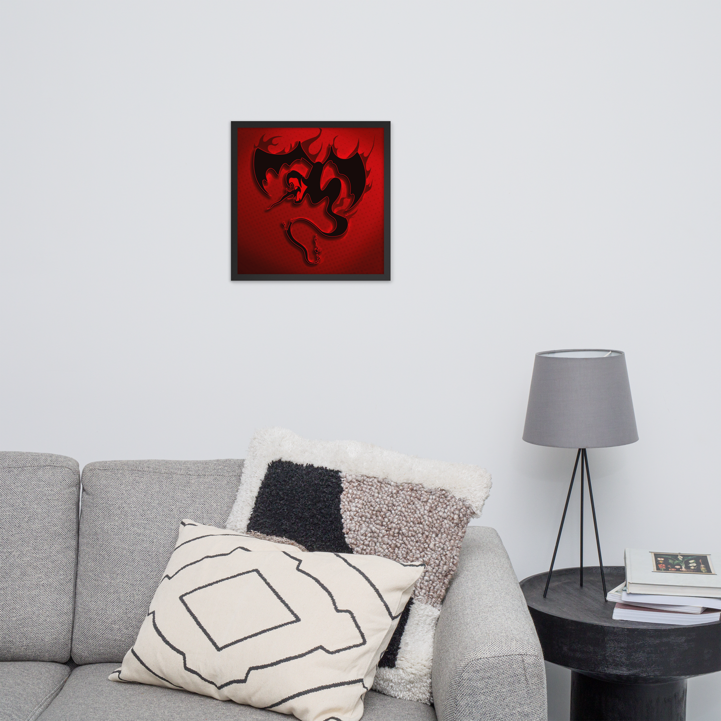 Framed firebreathing winged snake artwork with a red background and black design on a gray couch with decorative pillows.