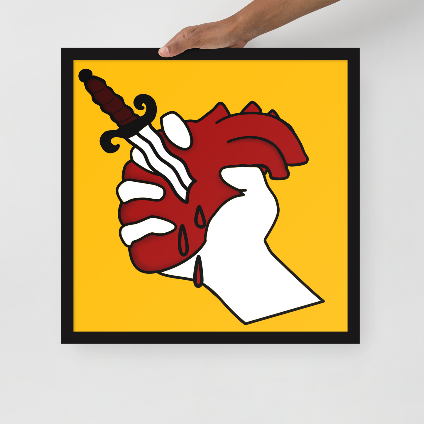 Framed artwork of a hand holding a heart with a dagger in it on a yellow background