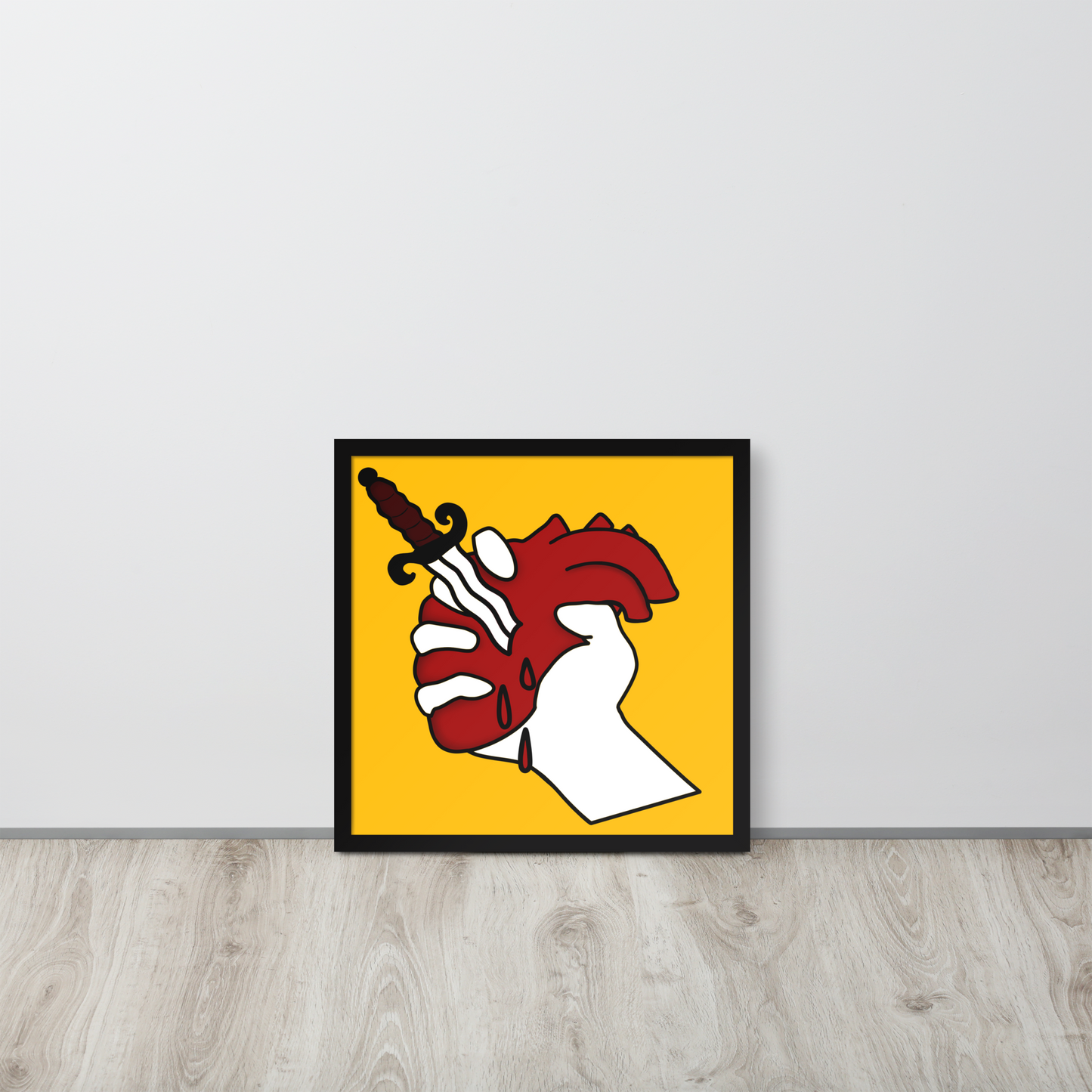 Framed artwork of a hand holding a heart with a dagger on a yellow background, leaning against a white wall.
