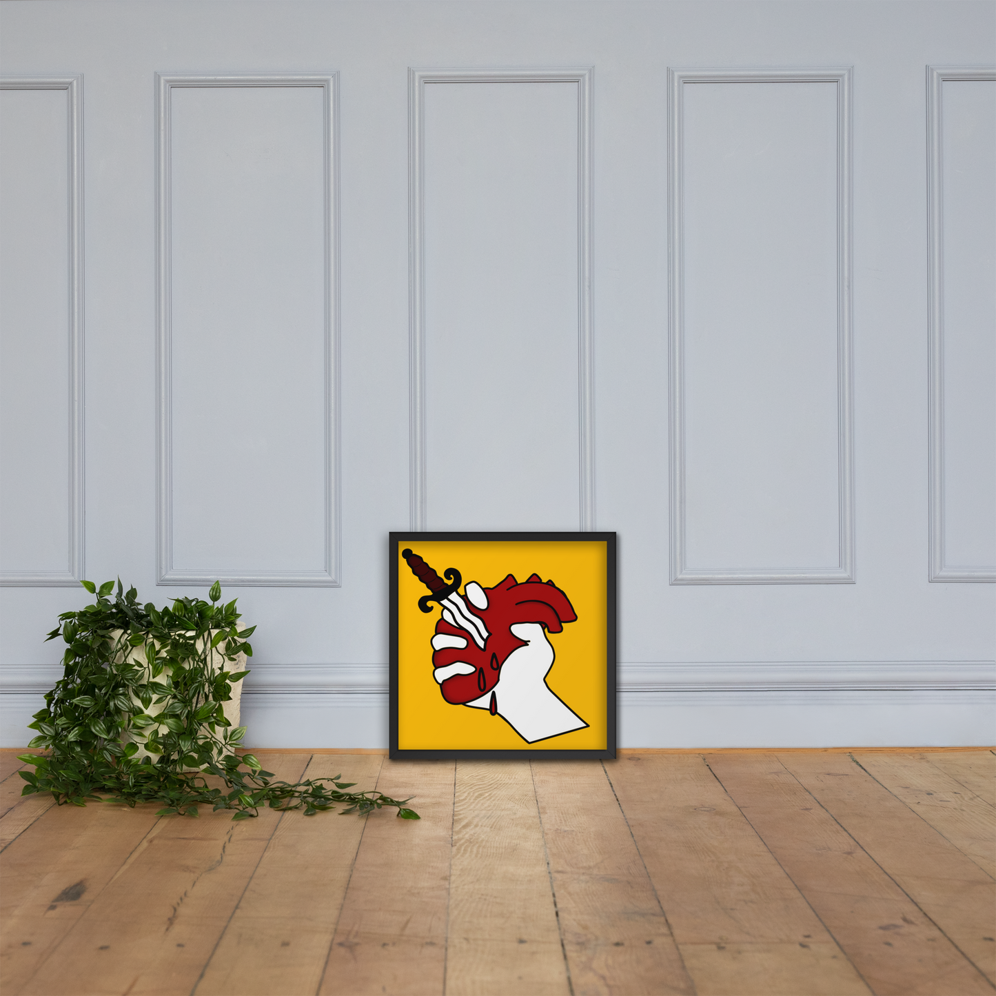 Framed heart stab artwork on a wall with a plant on a wooden floor