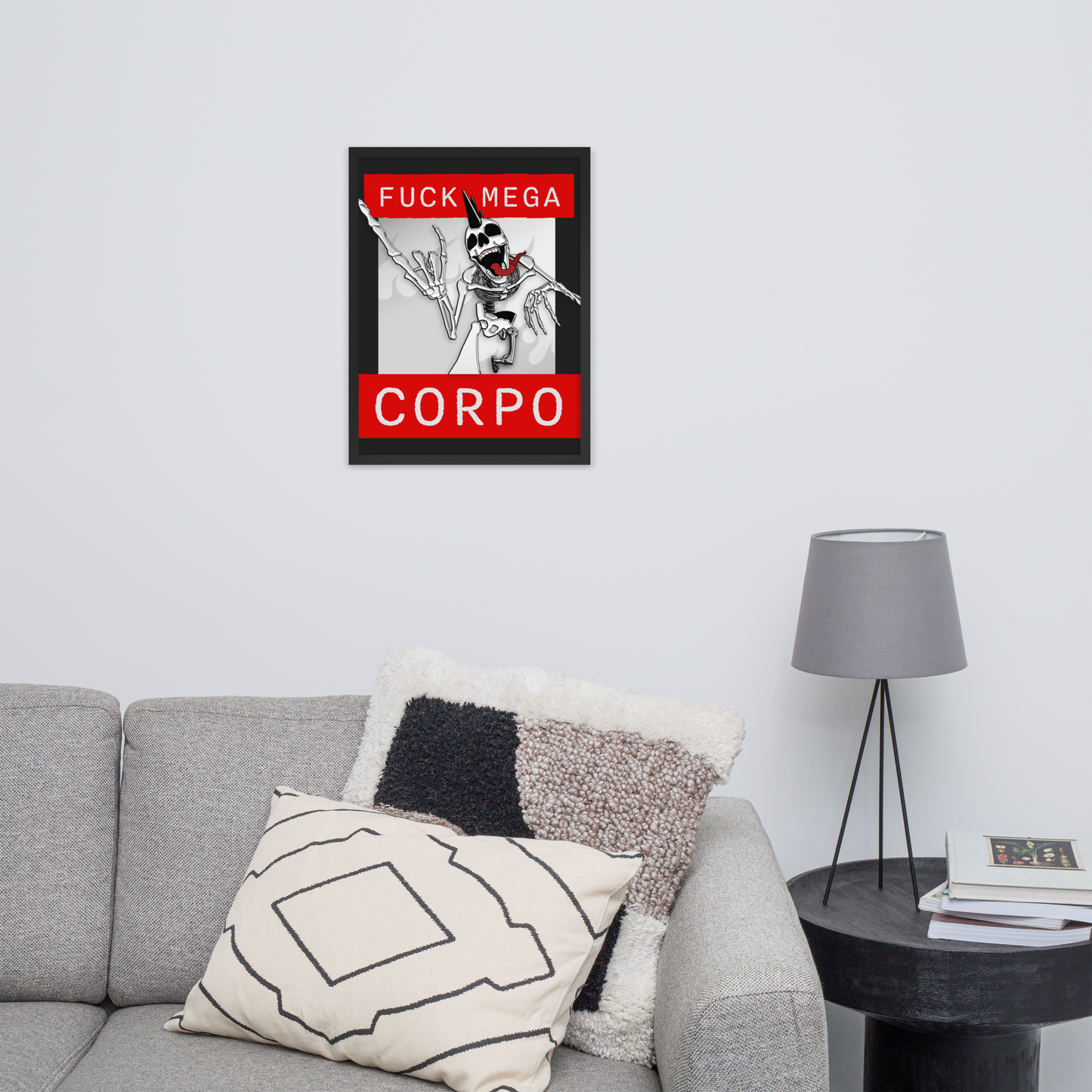 Framed 18x24 artwork of a heavy metal skeleton in front of 'FUCK MEGA CORPO' text with red, white, black, and grey coloration on a wall above a gray sofa with decorative pillows.