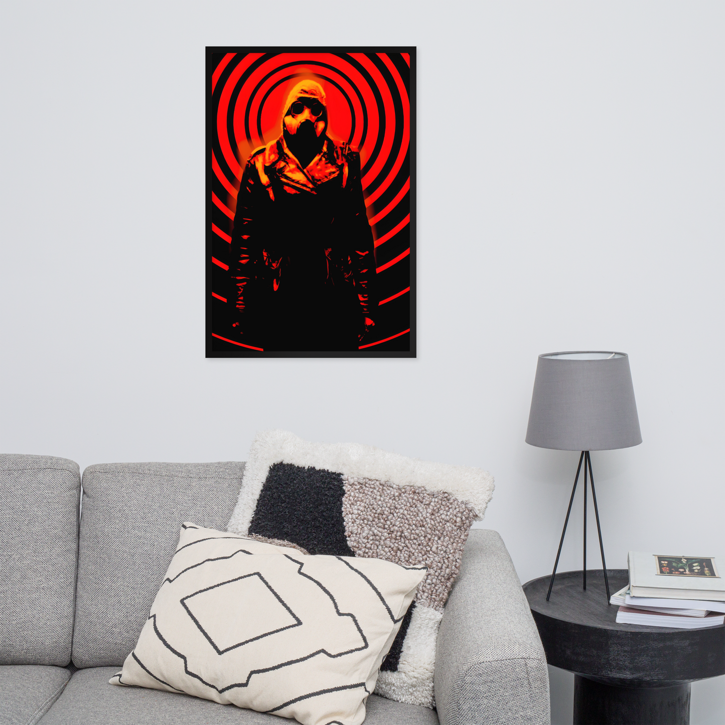 24x36 poster of a person in a red and black circular design on a wall above a gray couch with decorative pillows.