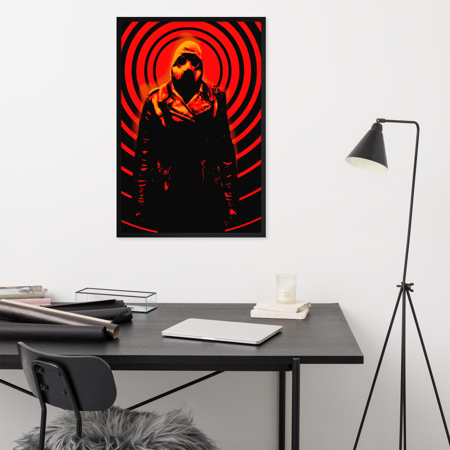 Poster of a a mysterious figure in a dark outfit with a hood and a gas mask against an orange and black circular background design on a wall above a desk.