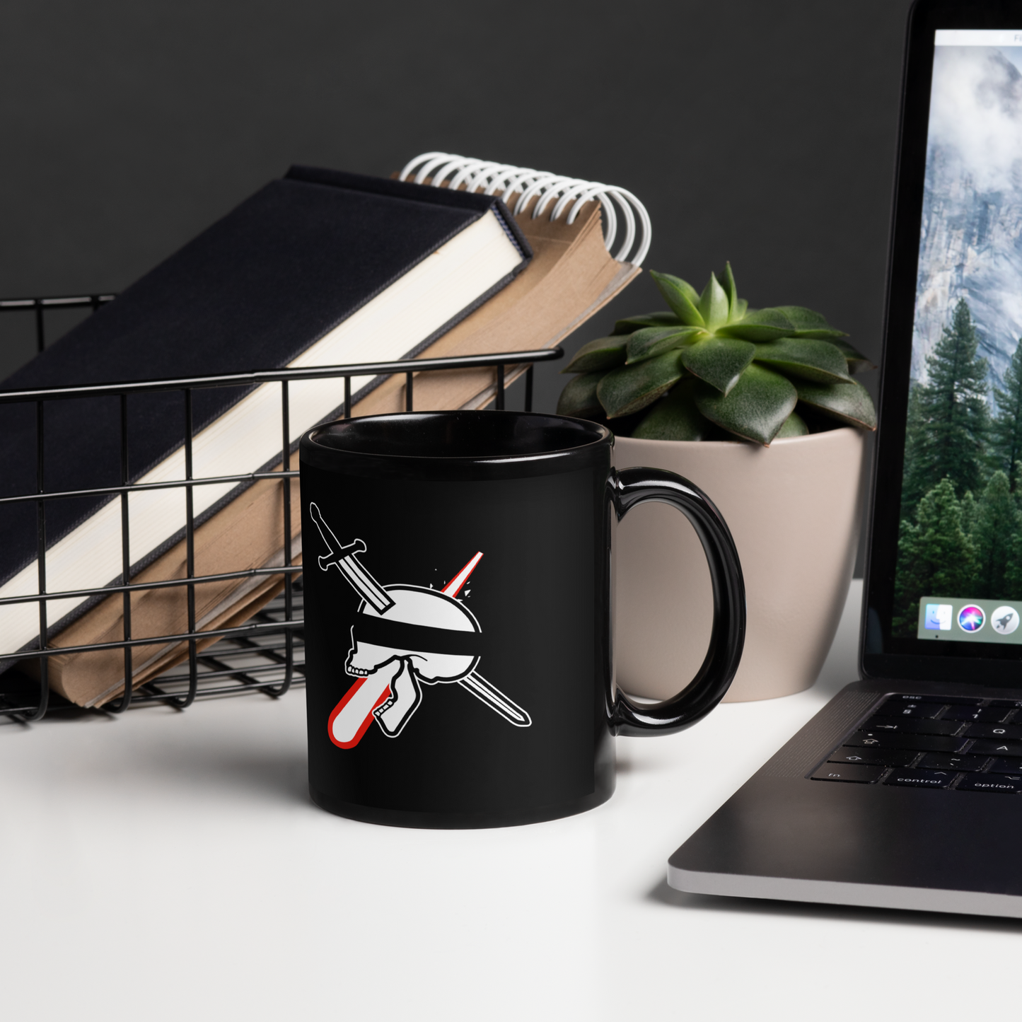 Black mug with a design on a desk next to a laptop and books