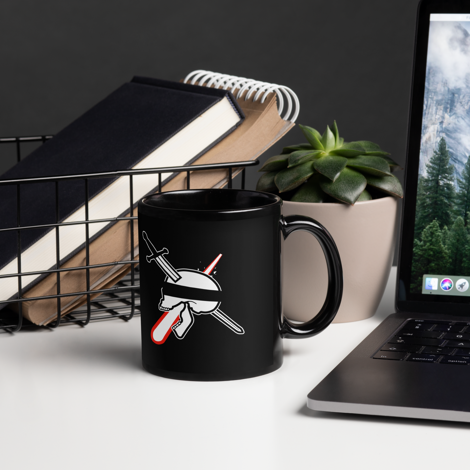 Black mug with a design on a desk next to a laptop and books
