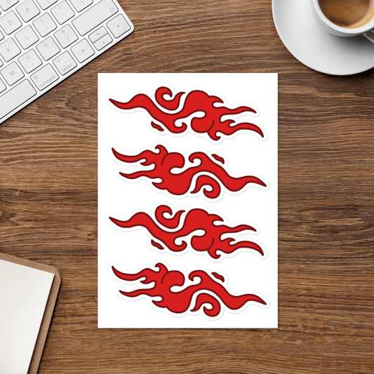 A sheet of four red flame-shaped decals or stickers on a white backing, placed on a wooden desk with a keyboard, coffee cup, and notebook partially visible around it.