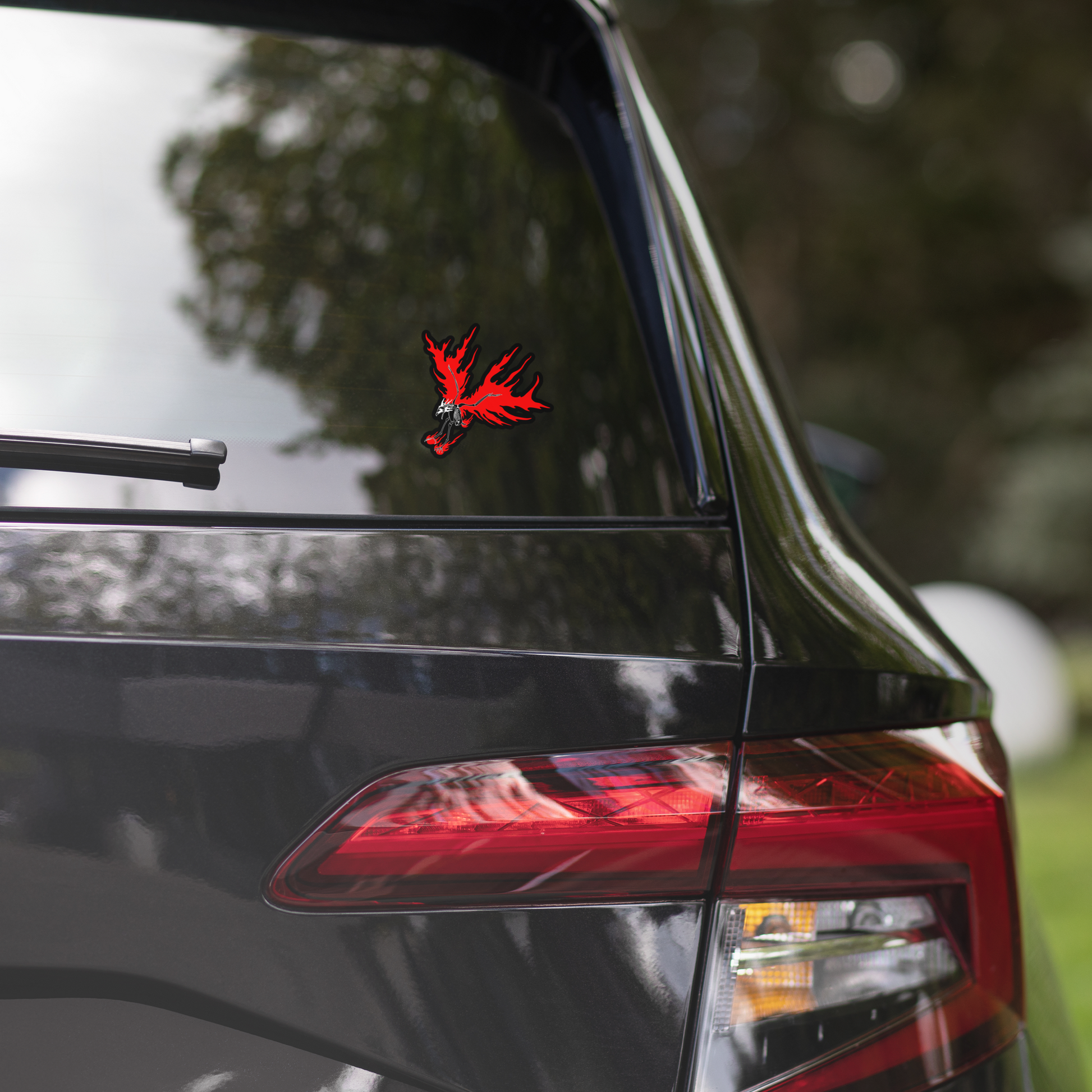 Car's rear window with a red and black decal, blurred greenery in the background