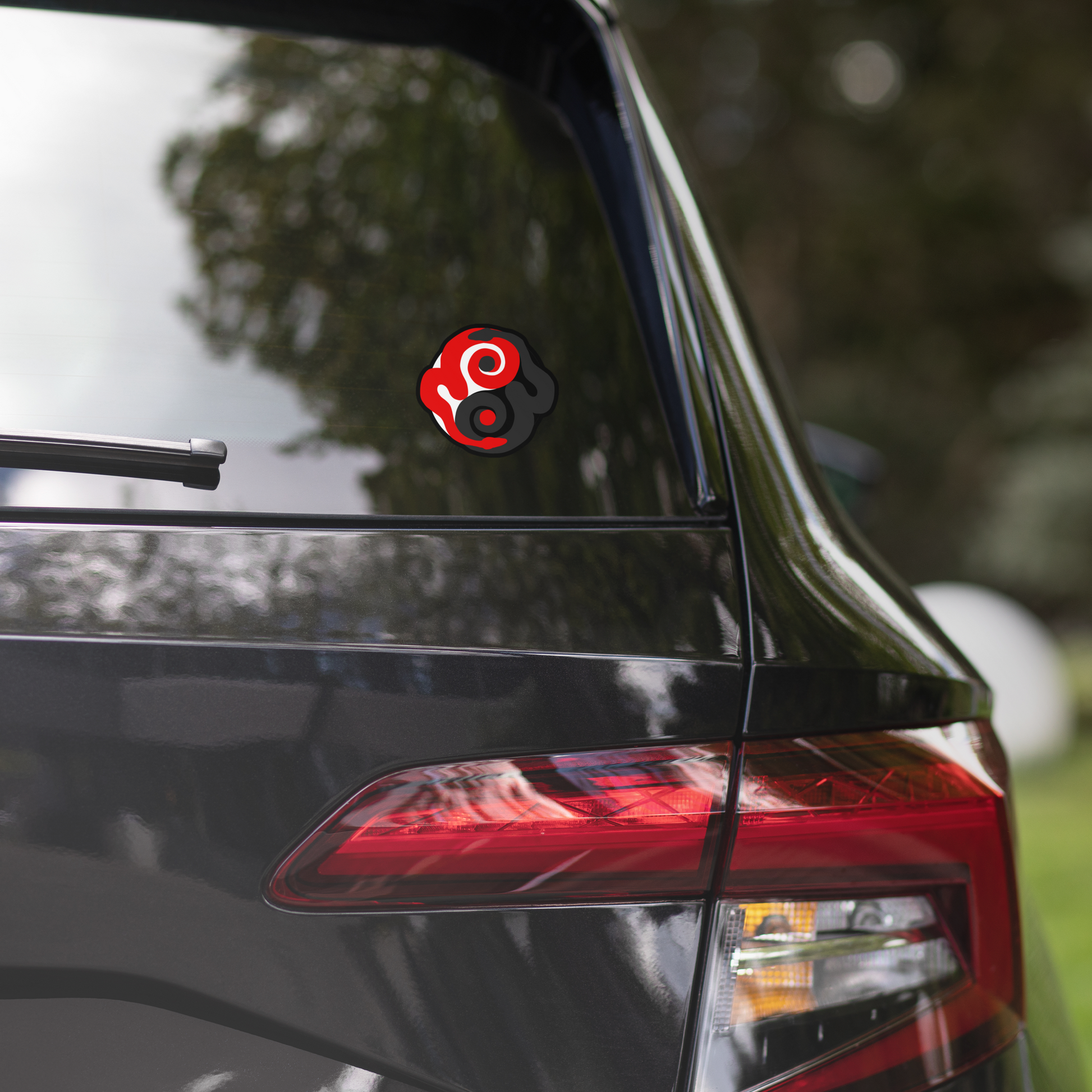 Car with a red and black circular decal on the back window, blurred greenery in the background