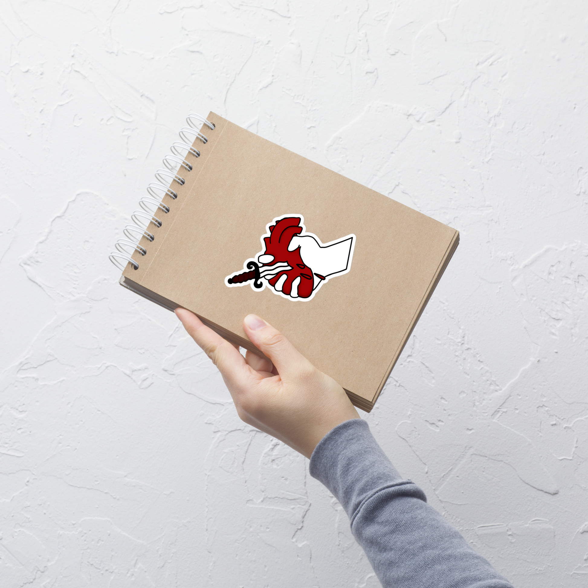 Hand holding a brown notebook with a red and white sticker on a light gray background