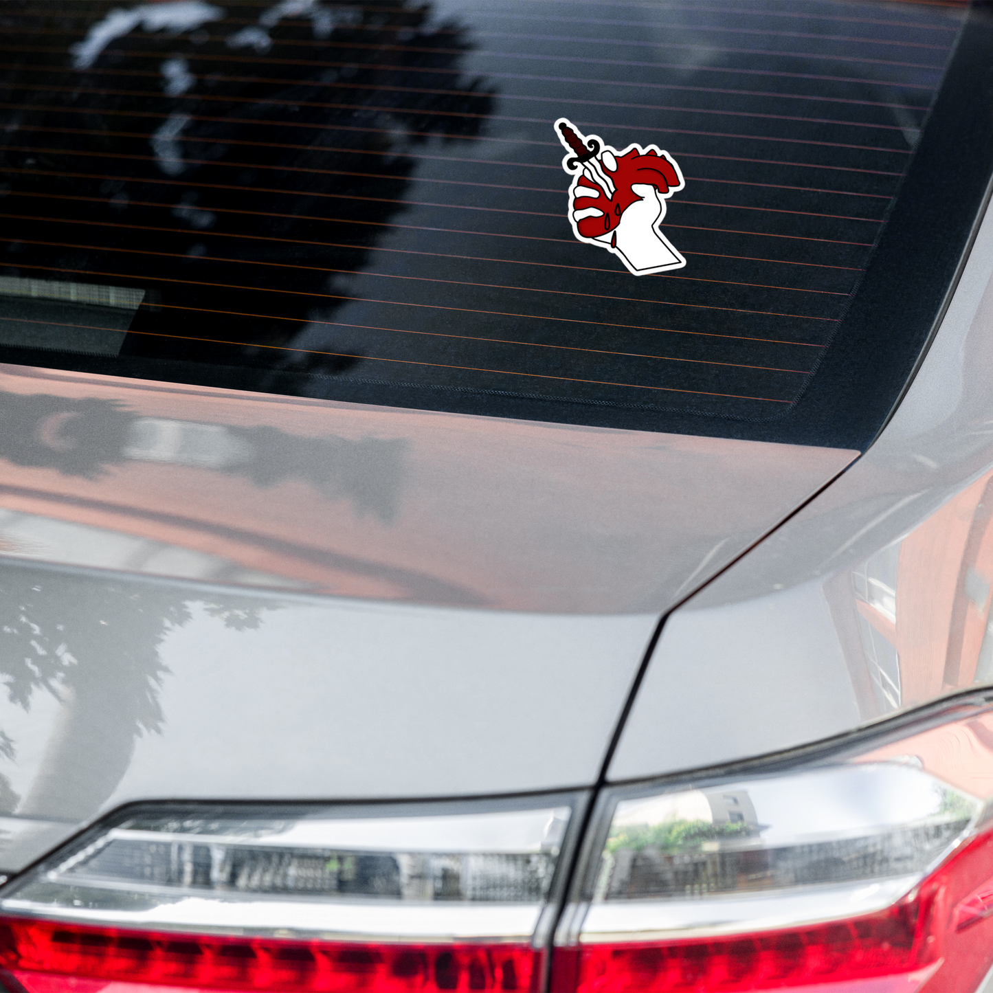 Car with a hand holding a dagger with a red heart in the background on a white background on the rear window