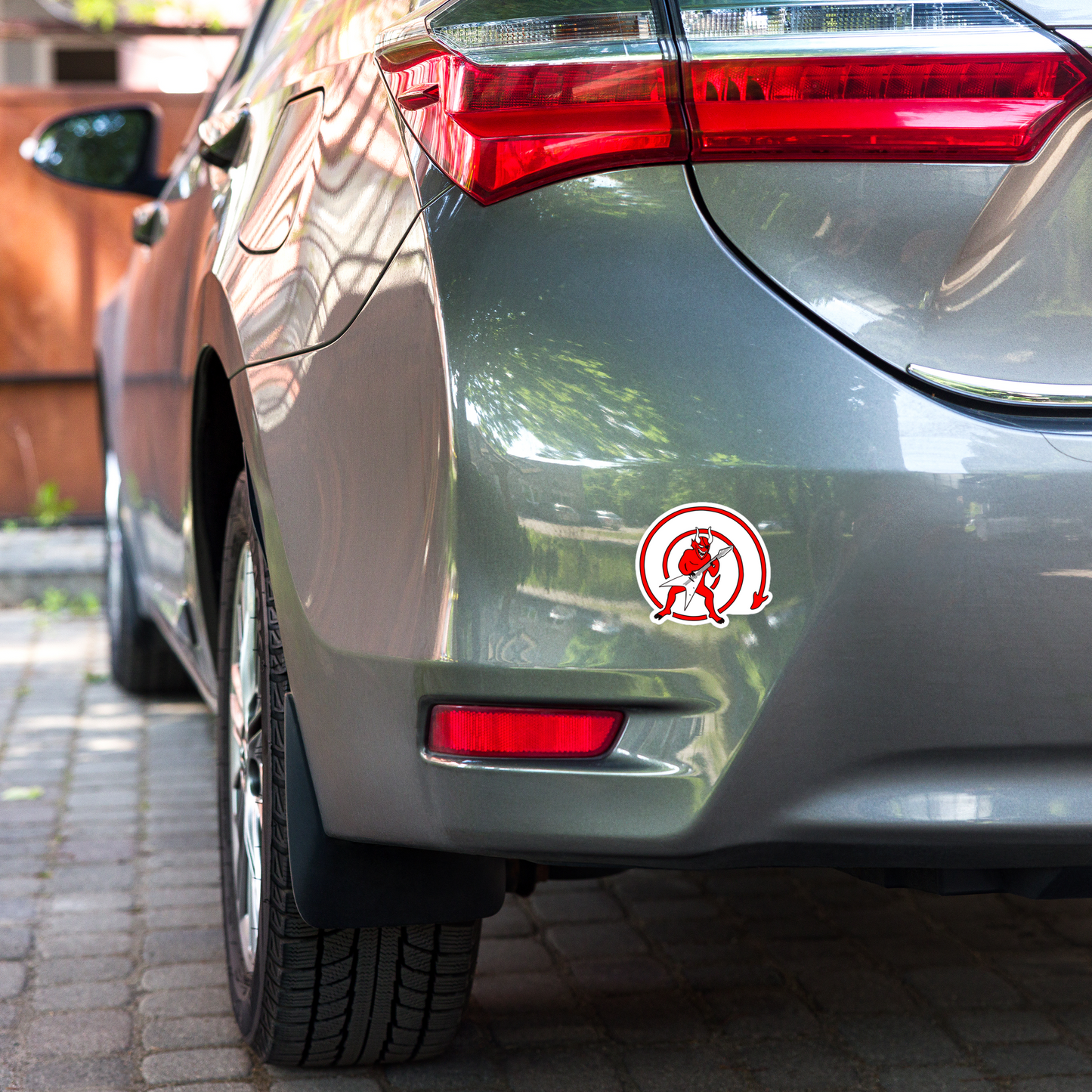 Car's rear end with a sticker of a red devil with a guitar inside a red circle on a white background on a blurred background