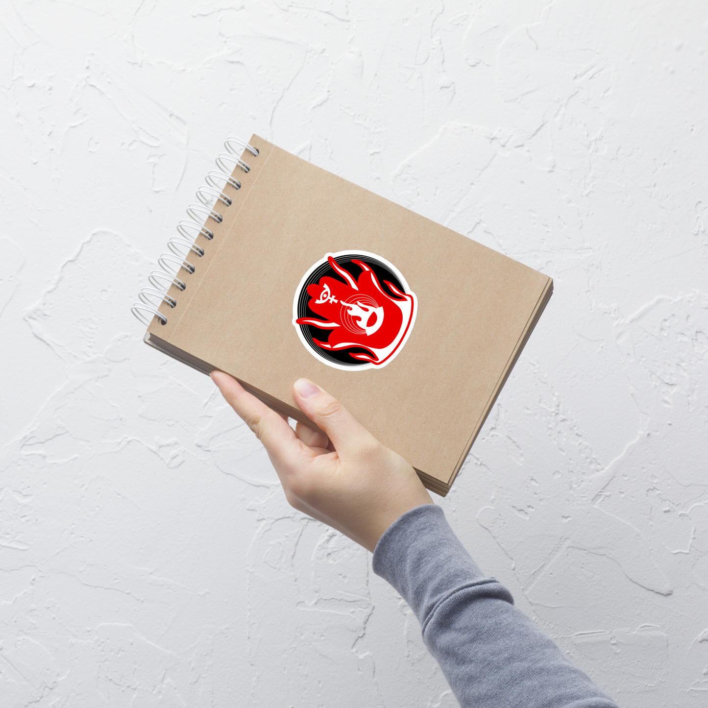 Hand holding a brown notebook with a red and black logo on a light gray background