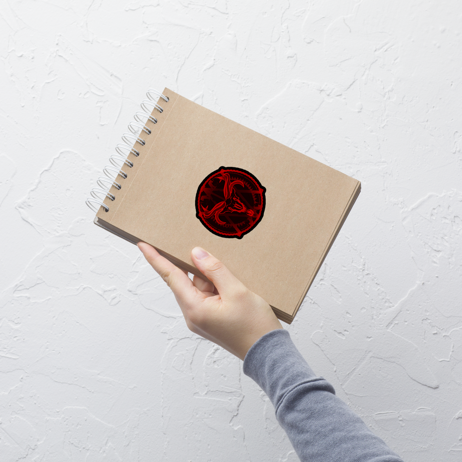 Hand holding a brown notebook with a red circular design on a light gray textured background