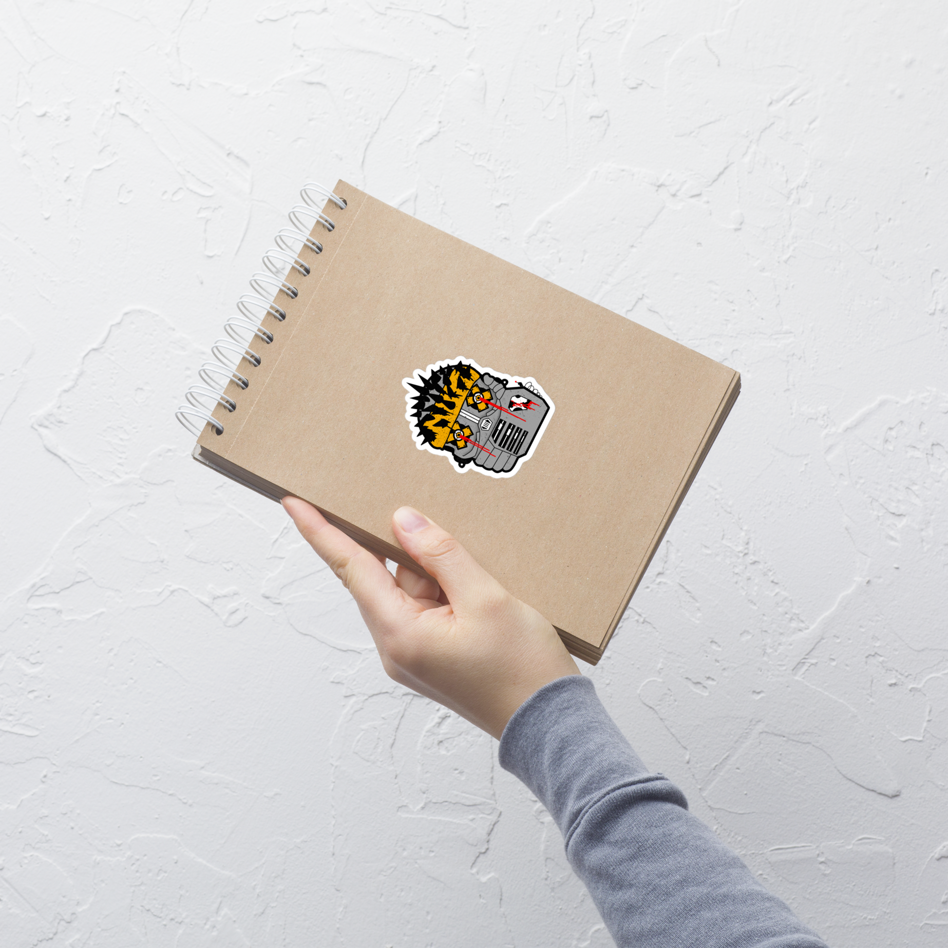 Hand holding a brown notebook with a sticker on a light gray textured background