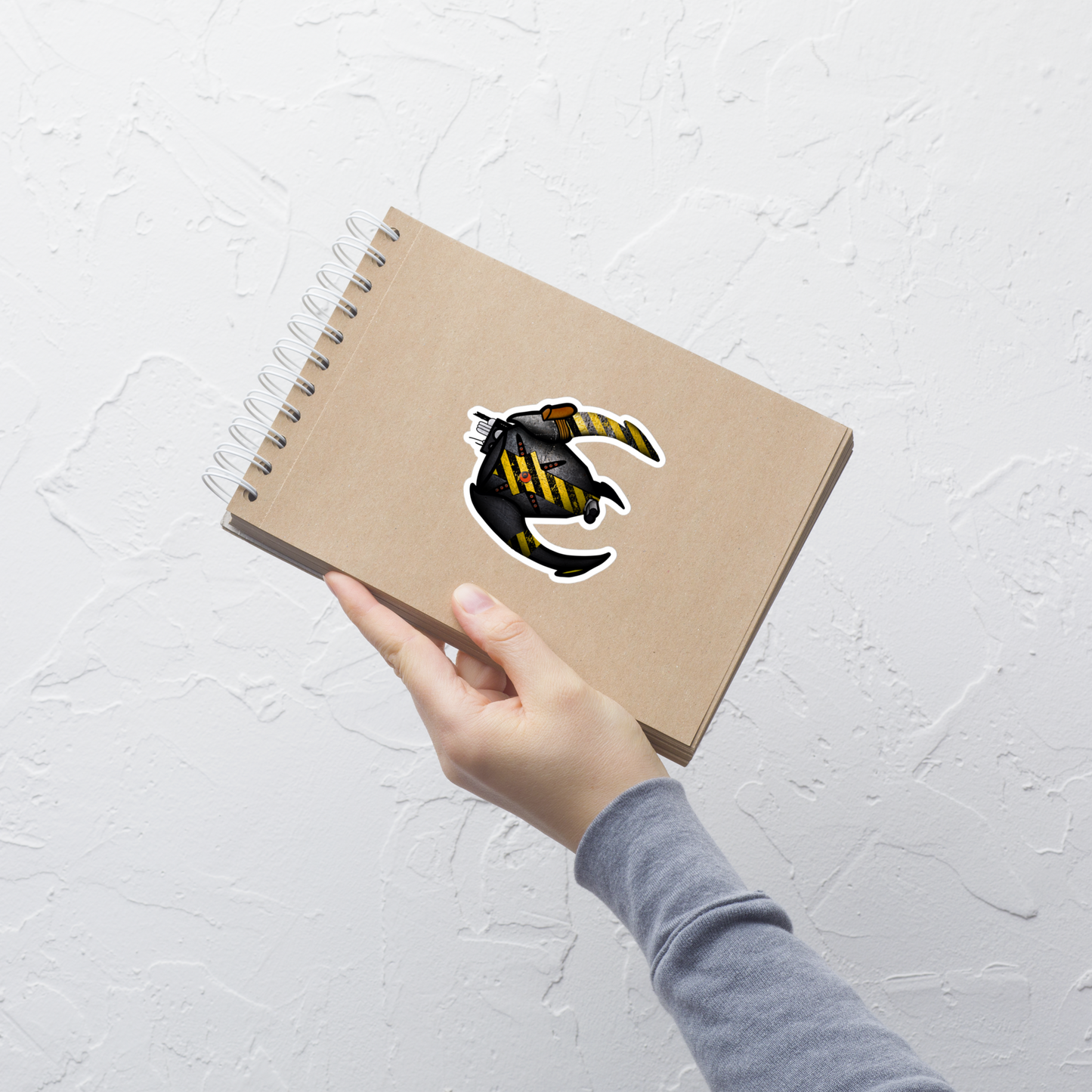 Hand holding a brown notebook with a logo on a light gray textured background