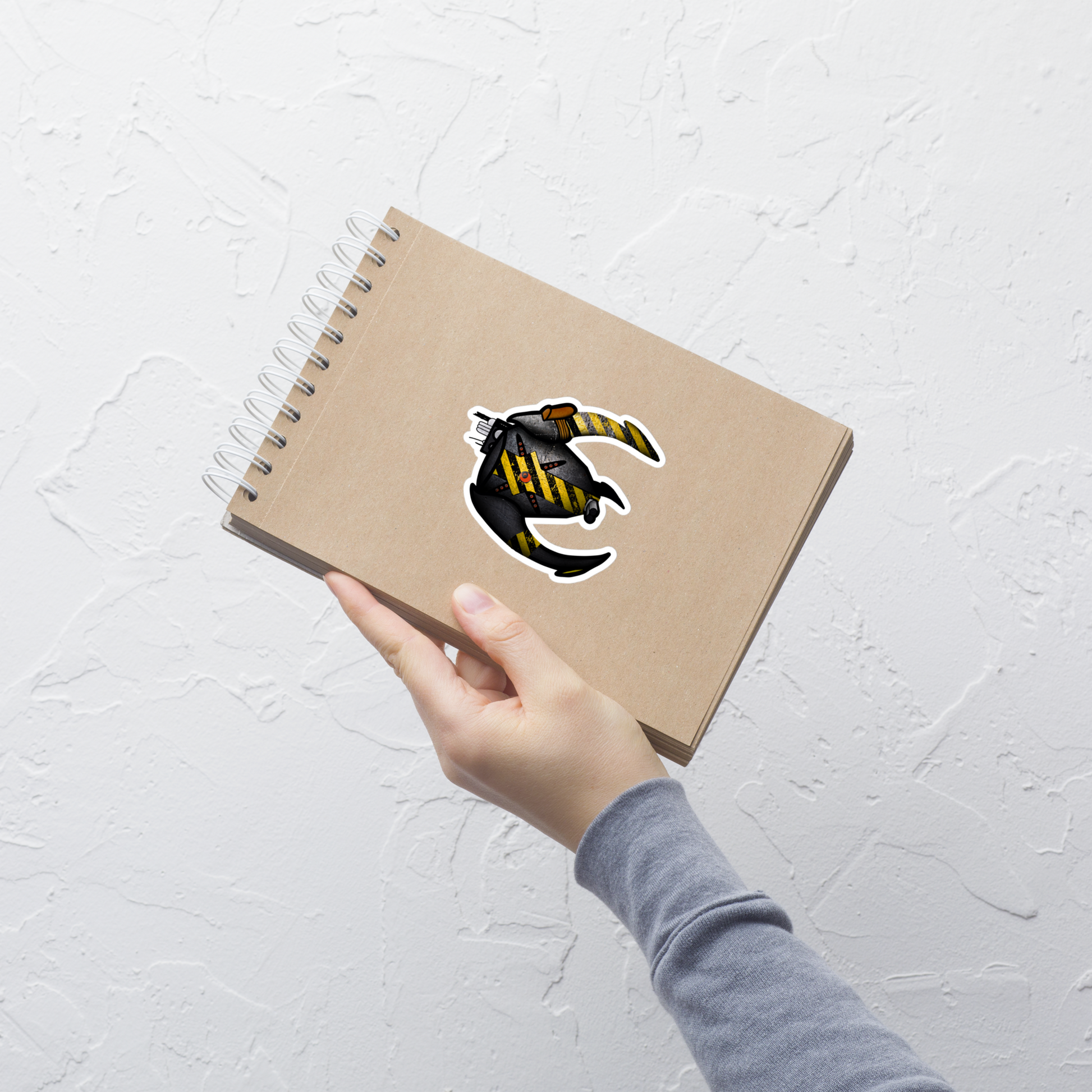 Hand holding a brown notebook with a logo on a light gray textured background