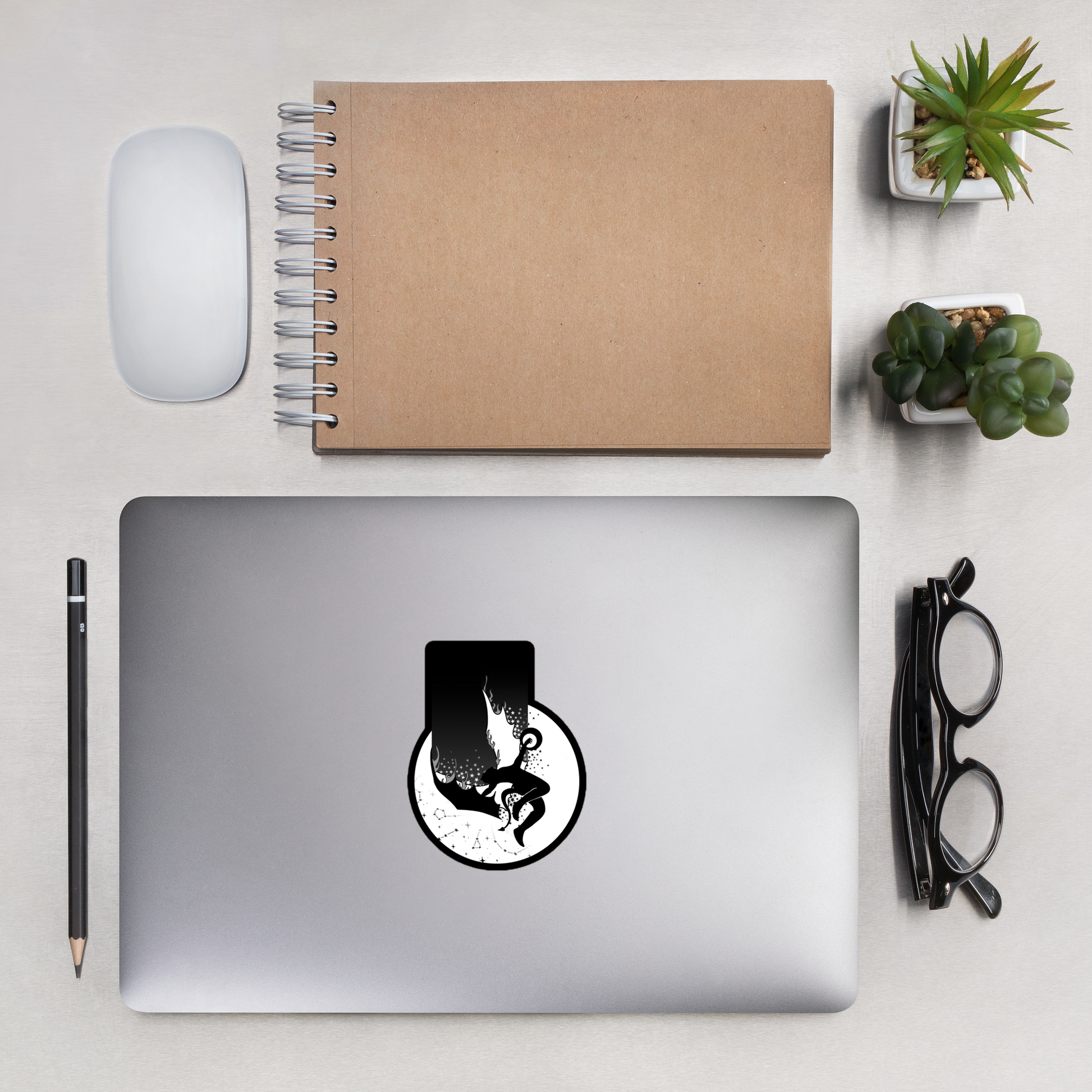 Laptop with a sticker on a desk with a notebook, mouse, and plants.