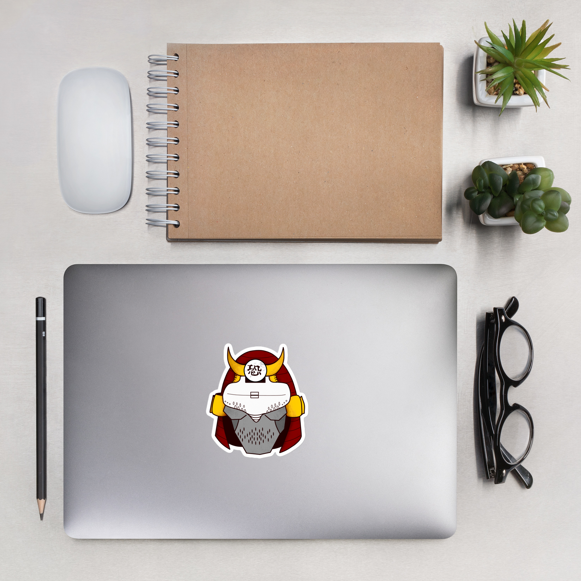 Laptop with a sticker on a desk with a notebook, mouse, pencil, and glasses.