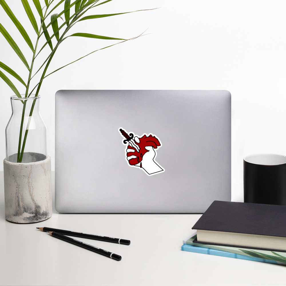 Laptop with a heart sticker with a dagger going through it on a desk with a plant, pencils, and books.
