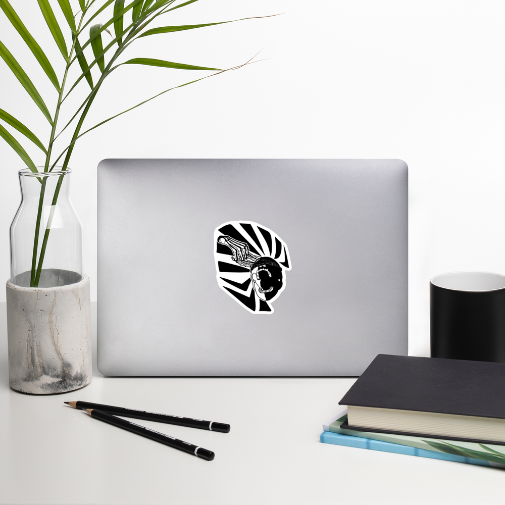 Laptop with a black and white graphic of a skeleton hand reaching upwards to pull thorns from his face in front of a sharp pattern in the background on a white surface with a plant, pencils, and books.
