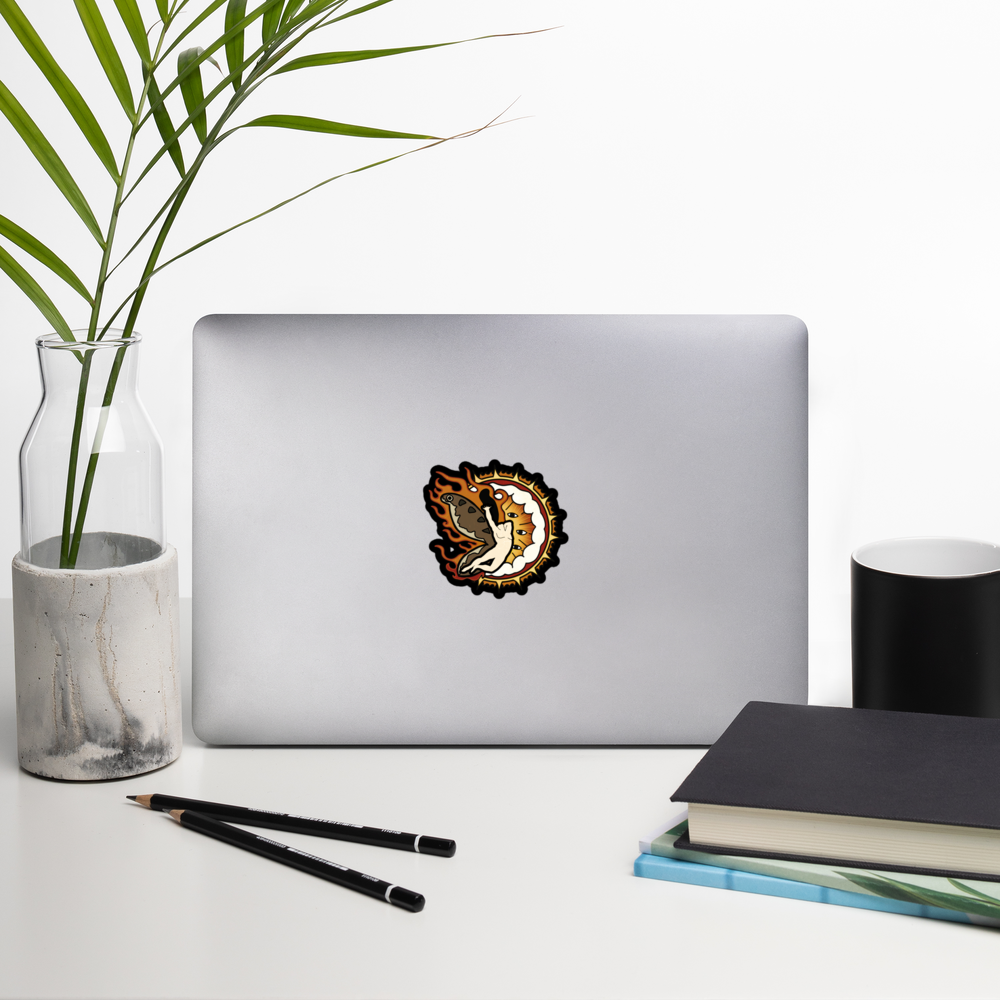 Sticker of a man with moth wings flying in front of a heavy metal biblical catholic design on a laptop behind a small stack of books next to a coffee mug and a potted plant