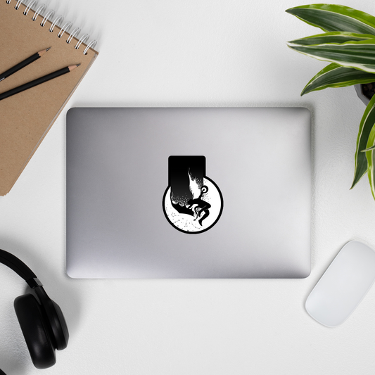 Laptop with a black and white sticker on a desk with a notebook, pencils, headphones, and a plant.