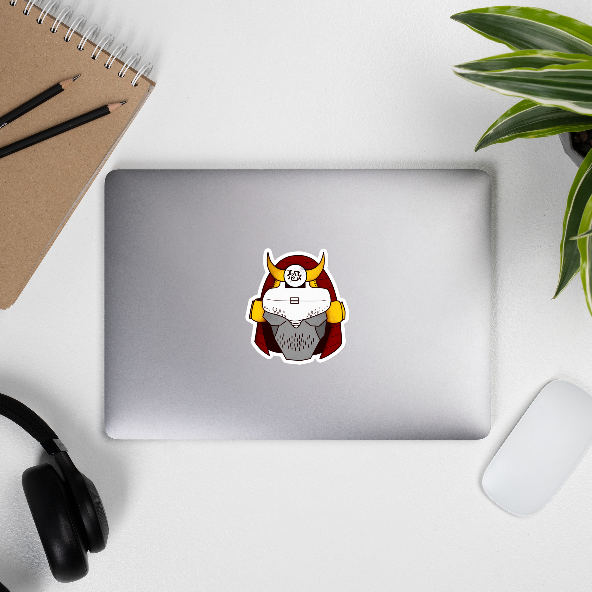 Cyberpunk samurai sticker with golden yellow flare and red helmet with overall warm color palette on a laptop by a mouse, headphones, potted plant, and journal with pencils on it