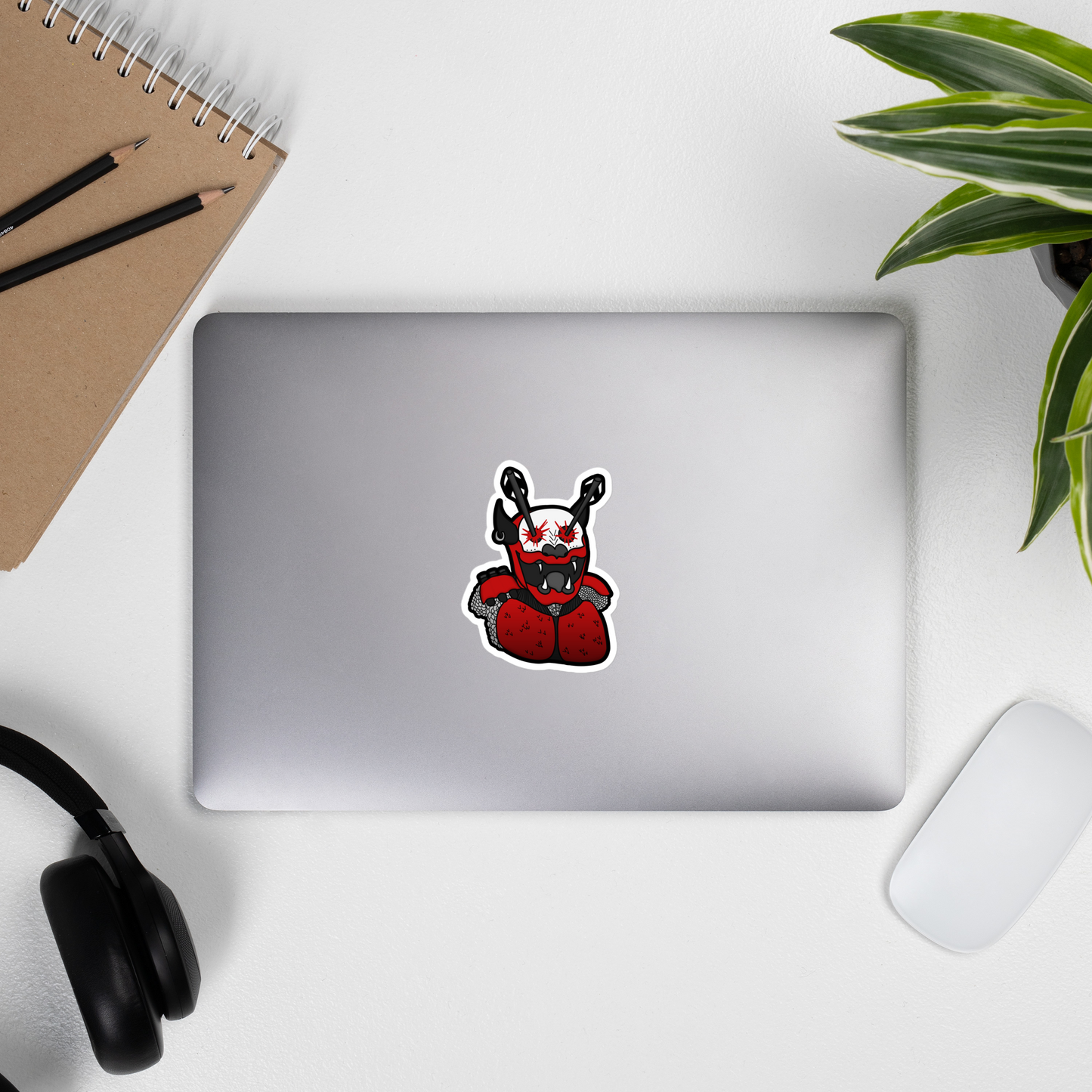 Laptop with a sticker on a desk with a notebook, pencils, headphones, and a plant.