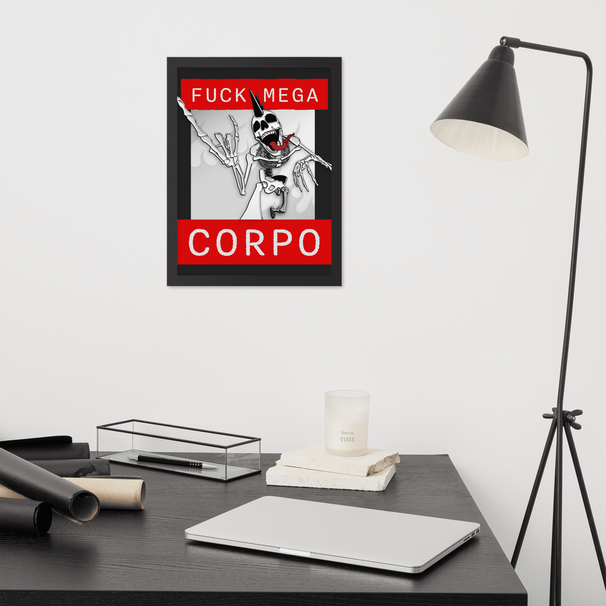Framed artwork of a heavy metal skeleton in front of 'FUCK MEGA CORPO' text with red, white, black, and grey coloration on a wall above a desk with office supplies.