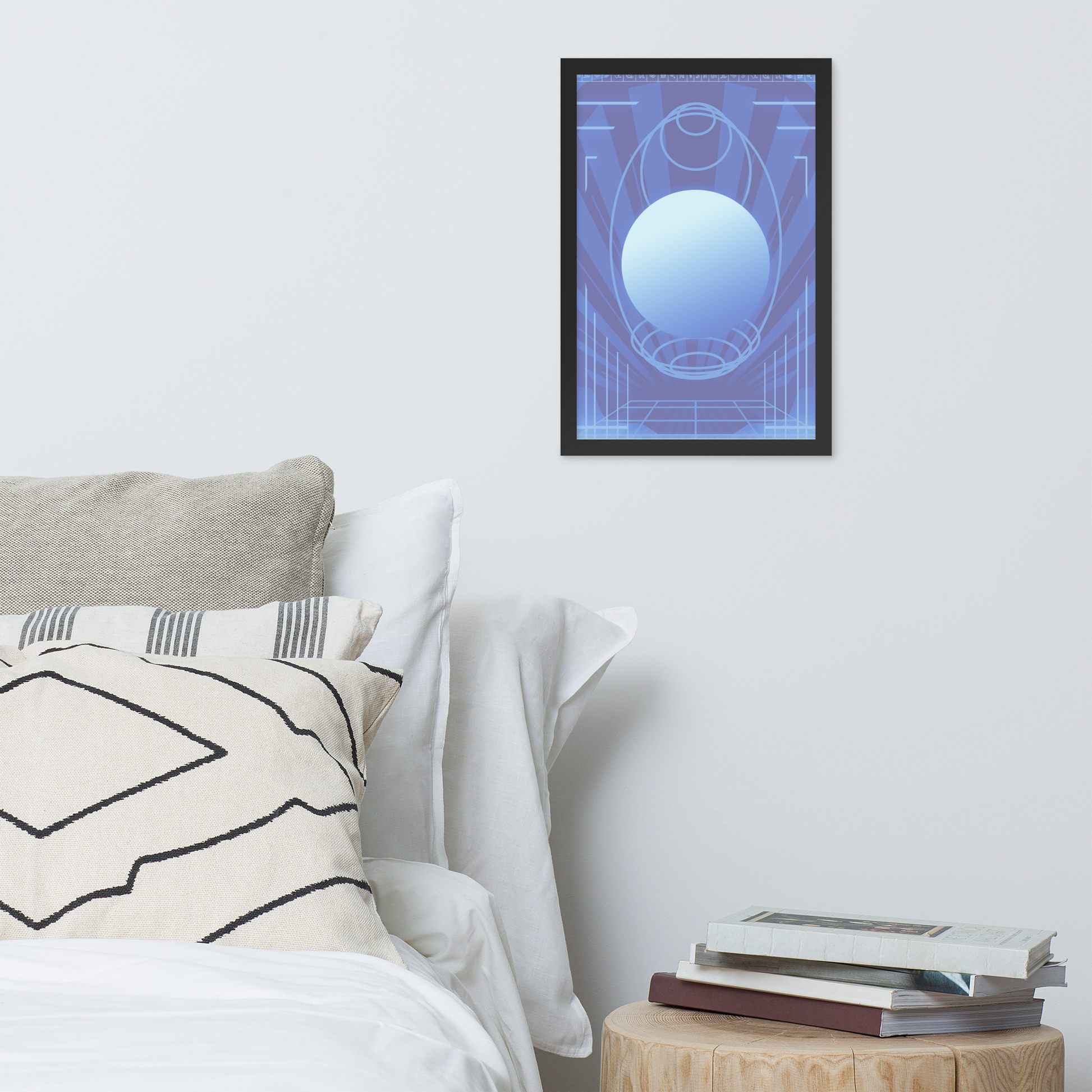 A framed abstract art print featuring a glowing blue sphere and geometric lines on a blue background, displayed on a light gray wall above a bed with pillows and a small wooden side table with books.
