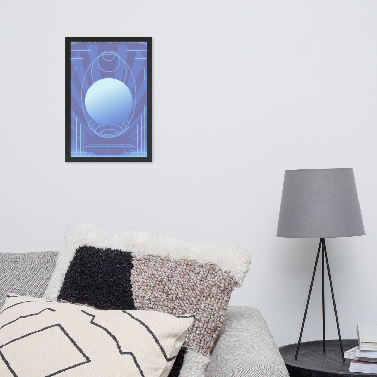 A framed abstract art print featuring a blue and purple geometric design with a central light blue sphere, displayed on a white wall above a sofa with textured pillows in a modern living room setting.