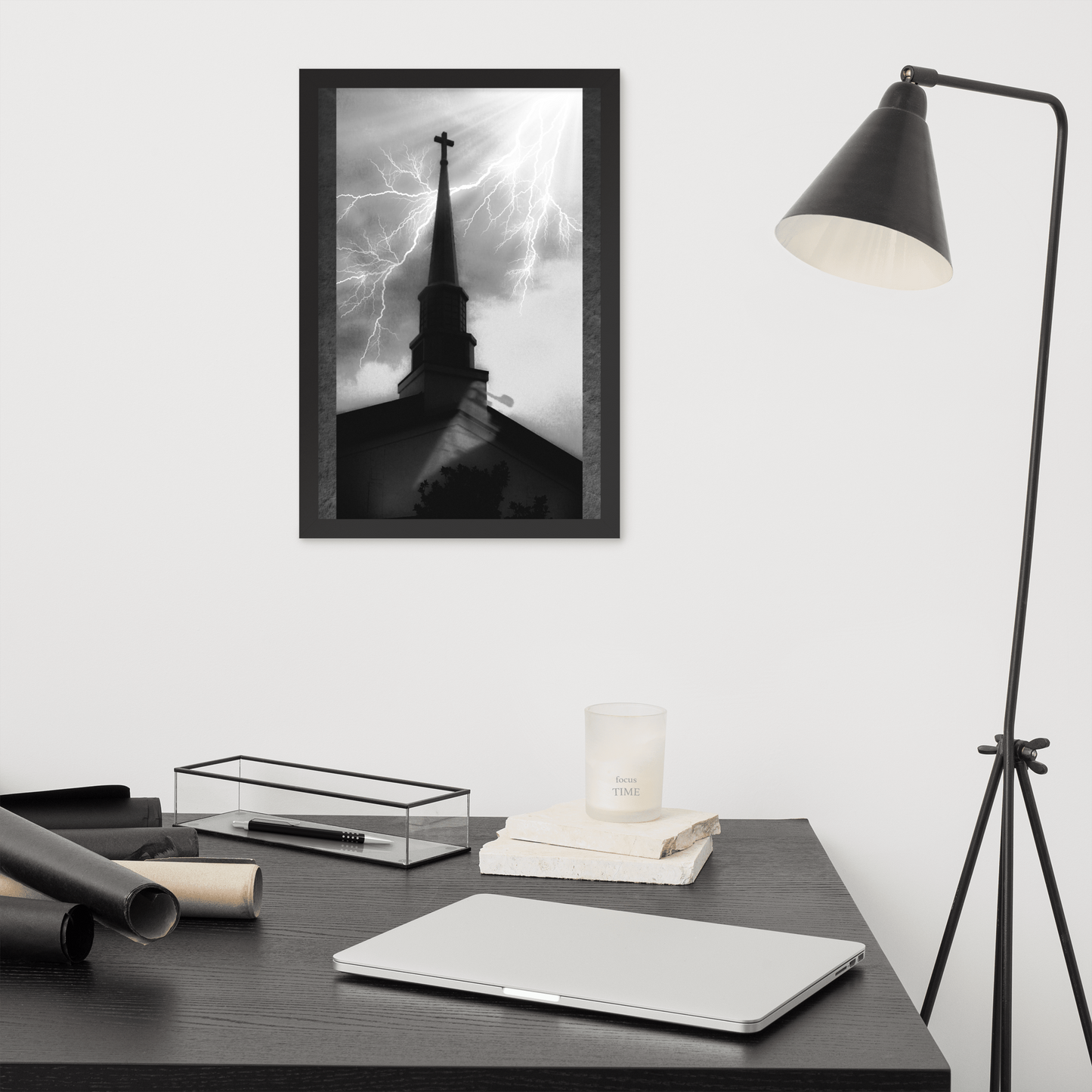 12x18 poster of a shadowy church in front of a lightning strike in grainy black and white heavy metal style hanging on a white wall over a black minimalist work station with a laptop and lamp