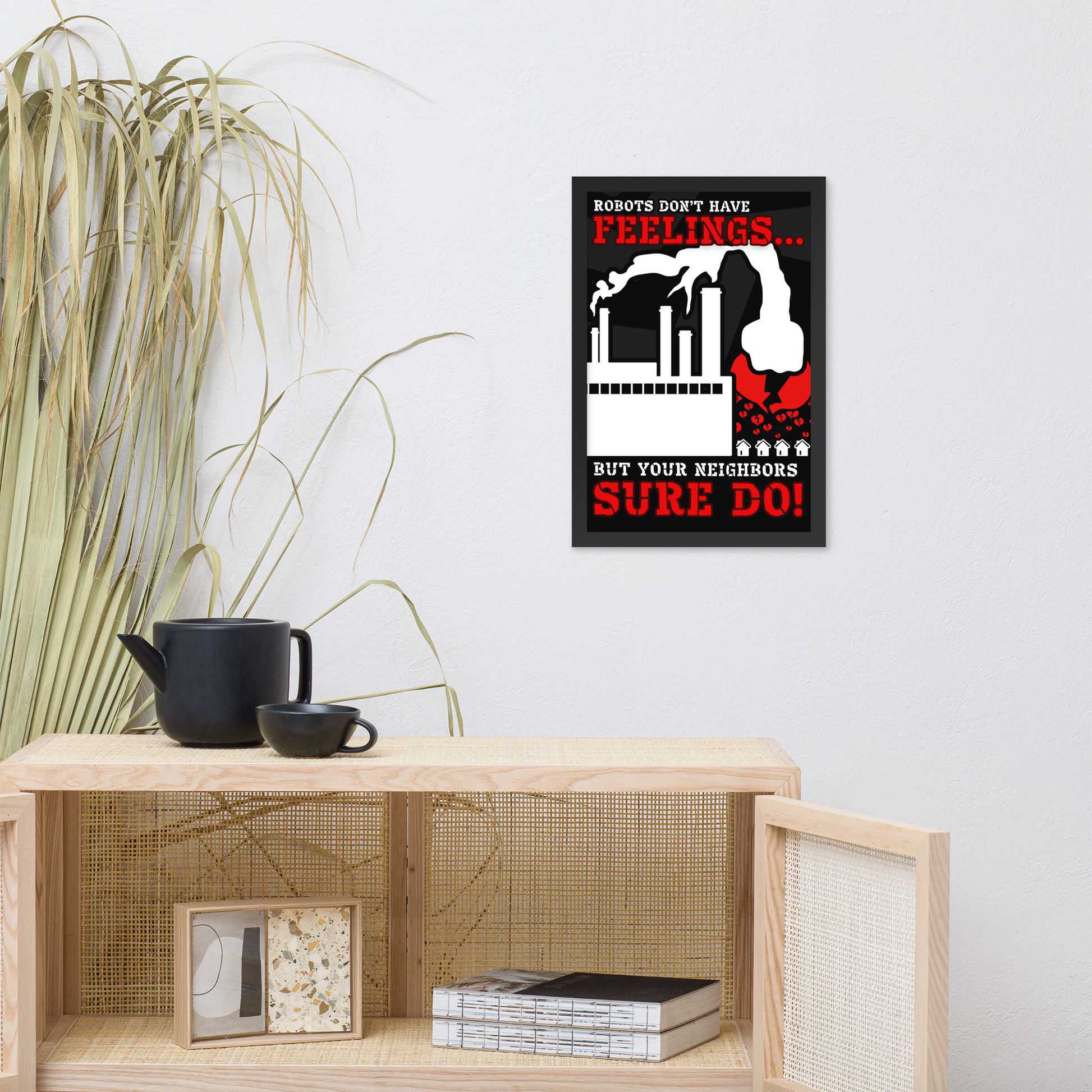 A framed wall art print with a black, white, and red sci-fi poster design hangs on a light gray wall above a wooden shelf. The print reads 'ROBOTS DON'T HAVE FEELINGS.