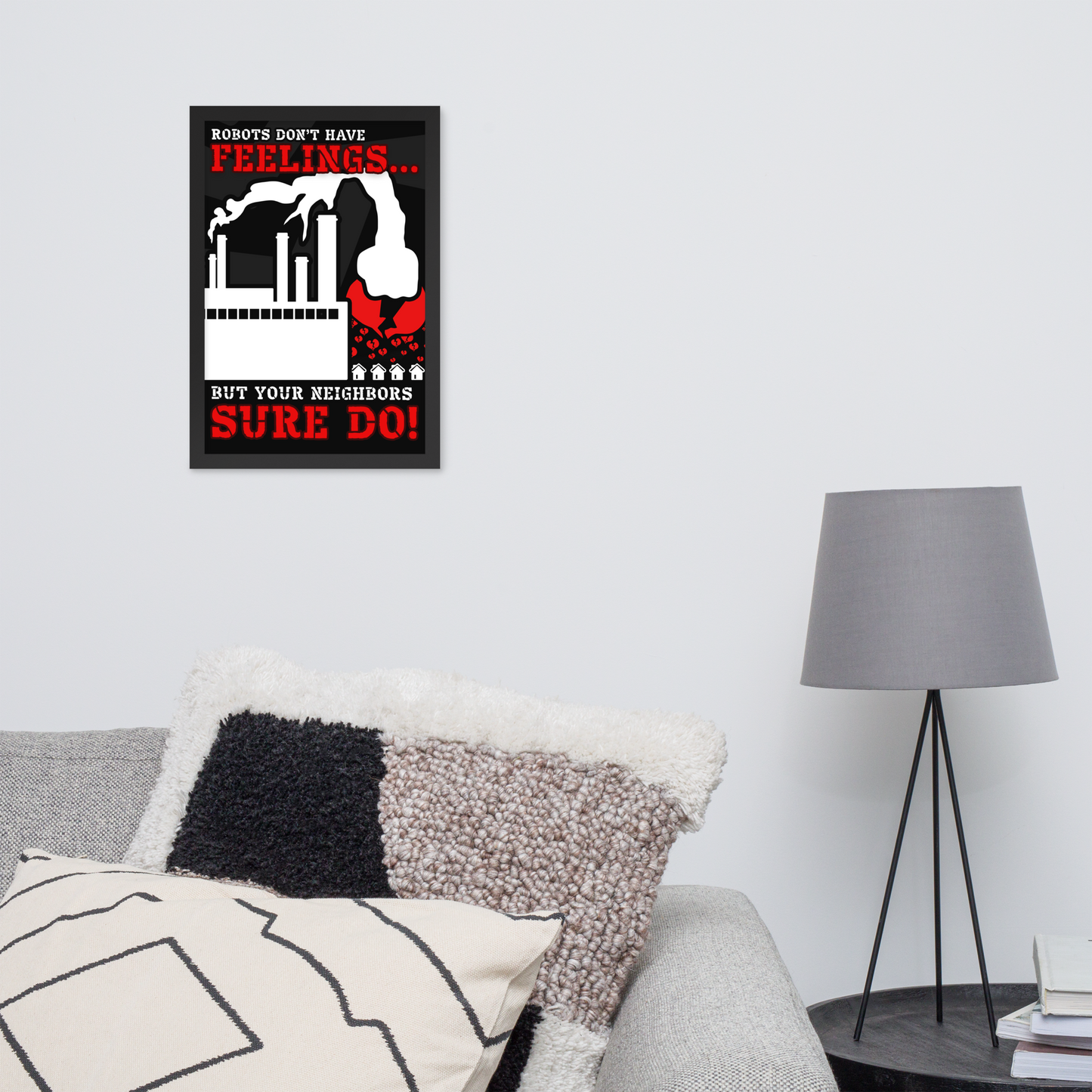 A framed wall art print with a black, white, and red graphic and text hangs on a light gray wall above a sofa with textured pillows, next to a gray floor lamp.