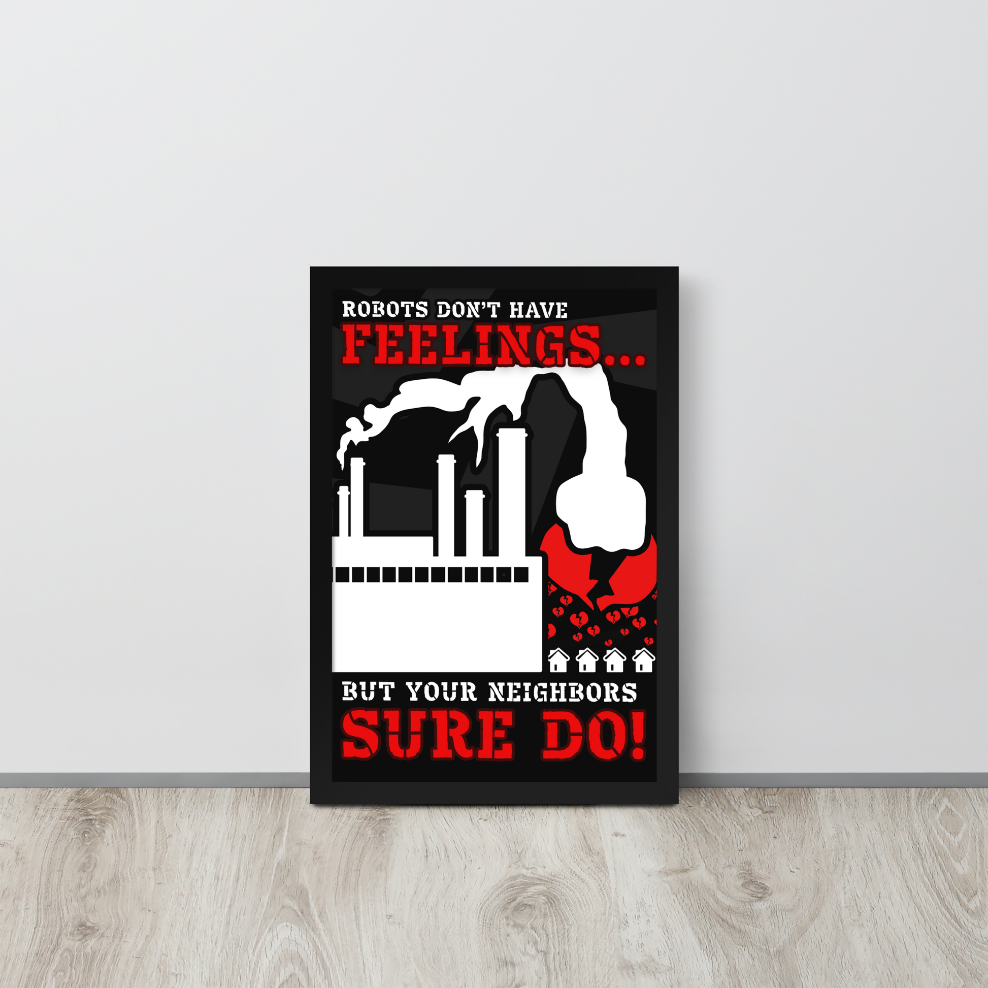 A framed wall art print leaning against a light gray wall on a light wood floor. The print features a black background with bold red and white text reading 'ROBOTS DON'T HAVE FEELINGS.