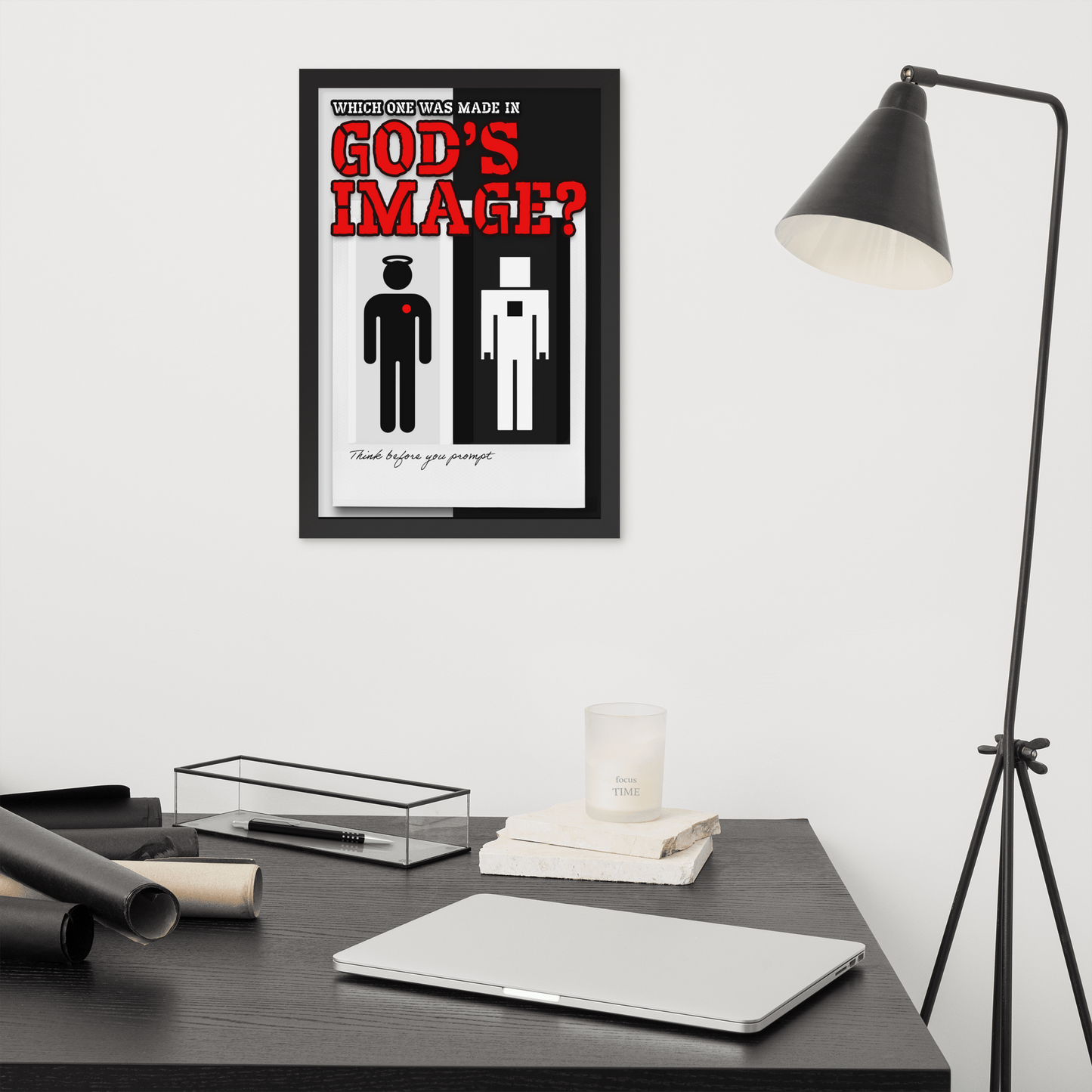A framed minimalist art print titled 'GOD'S IMAGE?' hangs on a white wall above a dark desk with a laptop, candle, and lamp nearby.