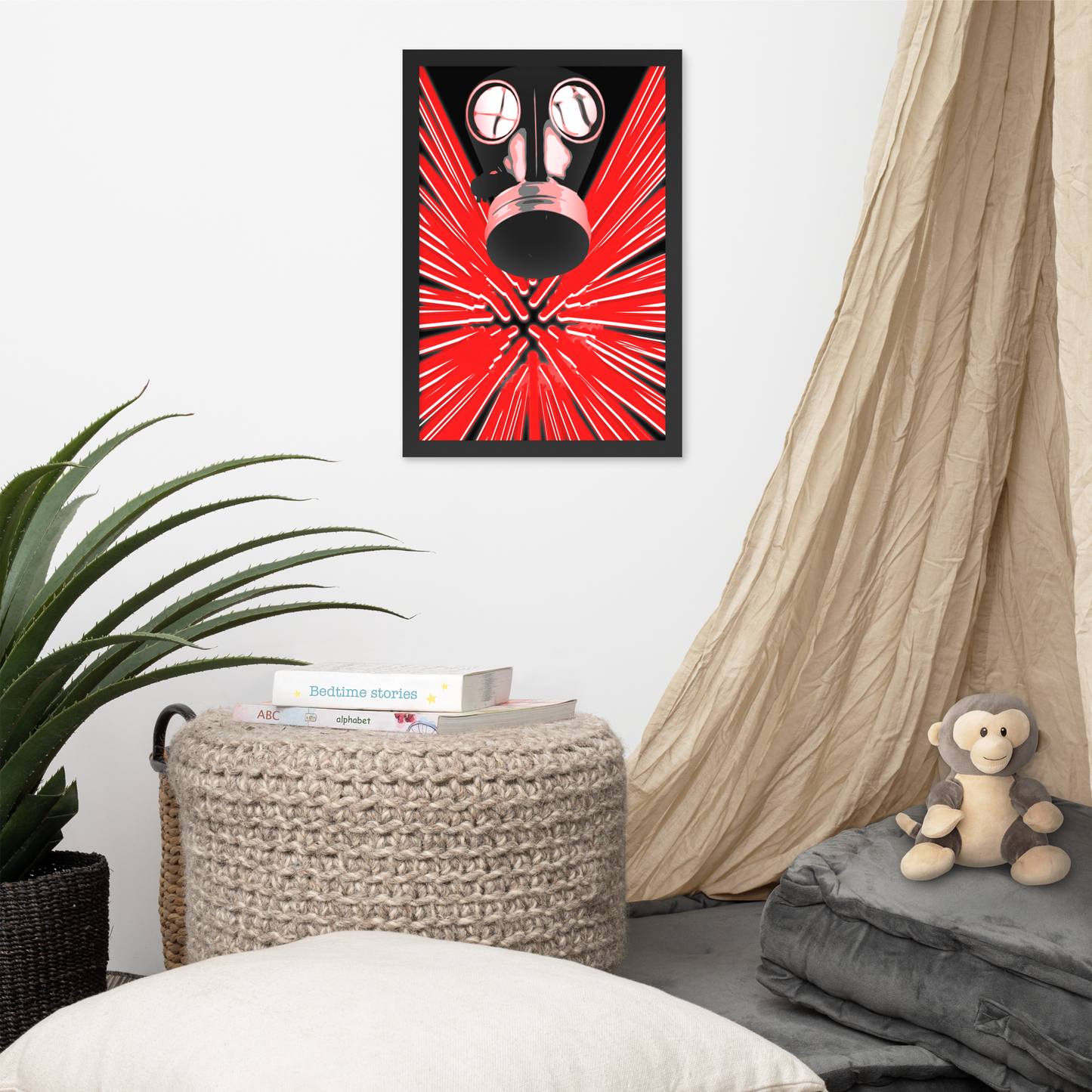 A framed wall art print featuring a black gas mask over a bright red radial burst pattern, displayed in a styled room setting with a woven ottoman, plant, draped fabric, and a plush monkey toy.