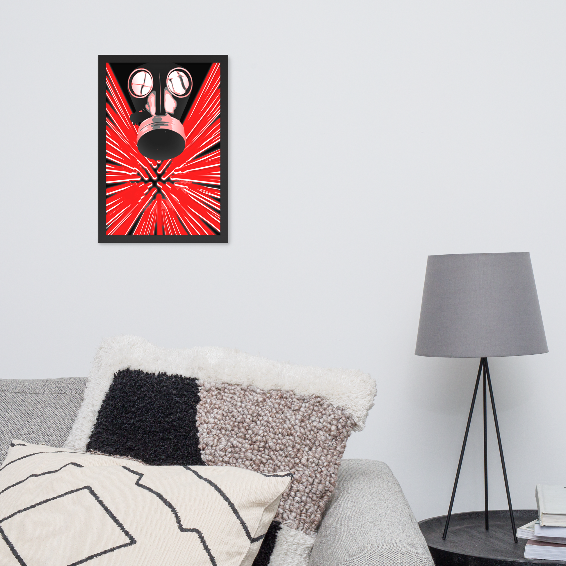 A framed wall art print featuring a stylized red and black gas mask with radiating red lines, displayed above a sofa in a modern living room setting with pillows and a gray floor lamp.