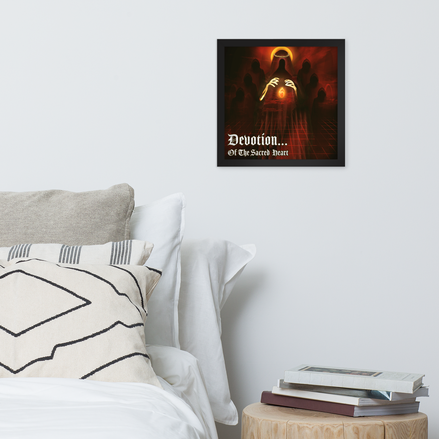 Framed artwork titled 'Devotion... Of The Sacred Heart' above a bed with pillows and books on a nightstand.