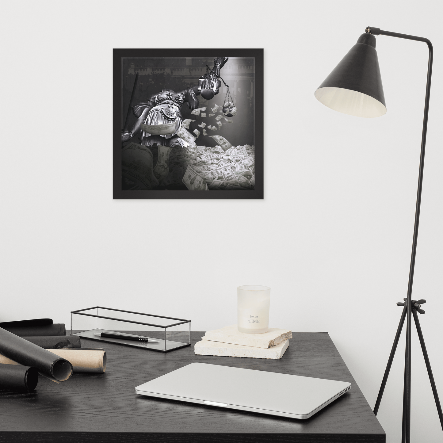 Framed artwork on a wall above a desk with a laptop and lamp.