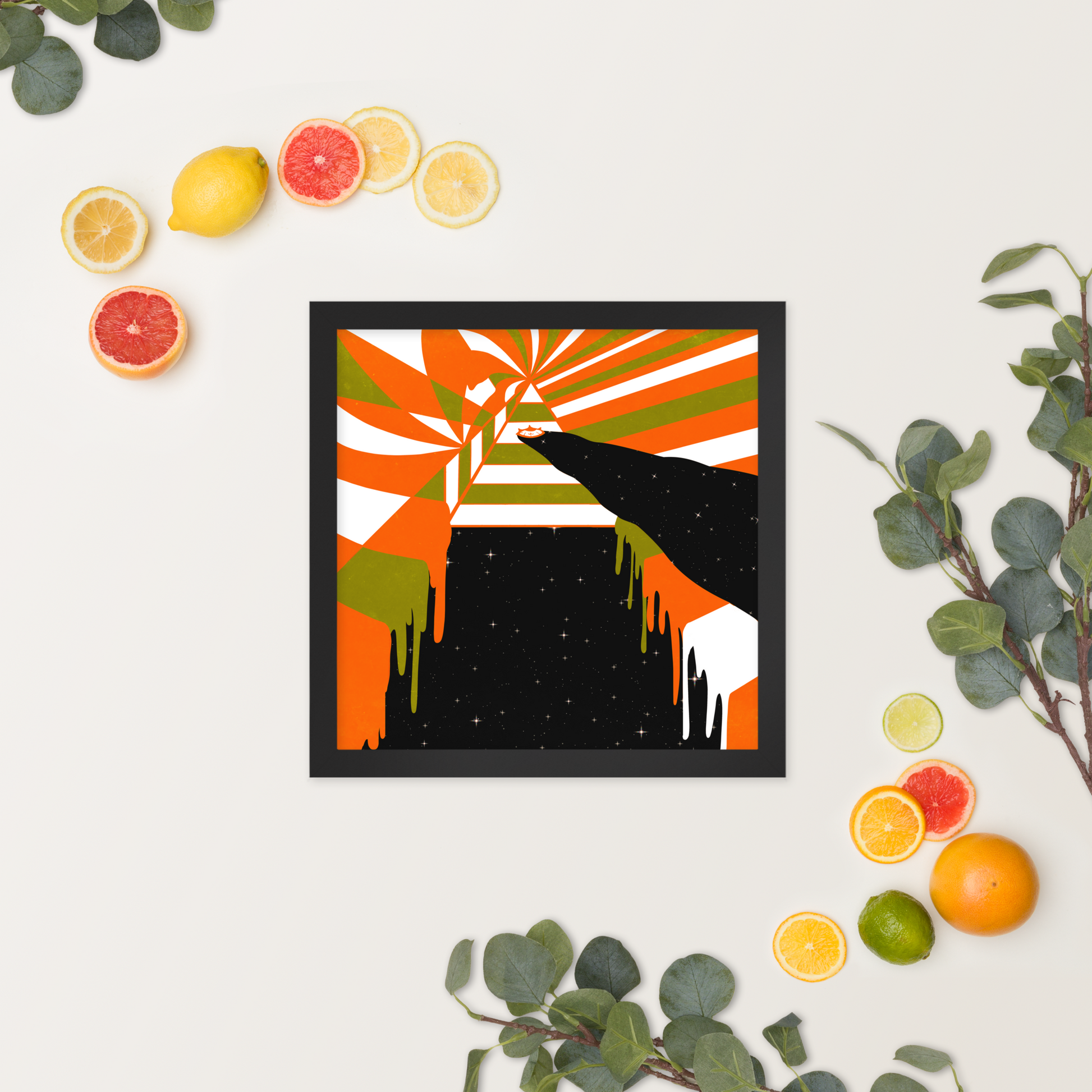 Framed abstract artwork with a colorful design on a white surface surrounded by citrus fruits and green leaves.