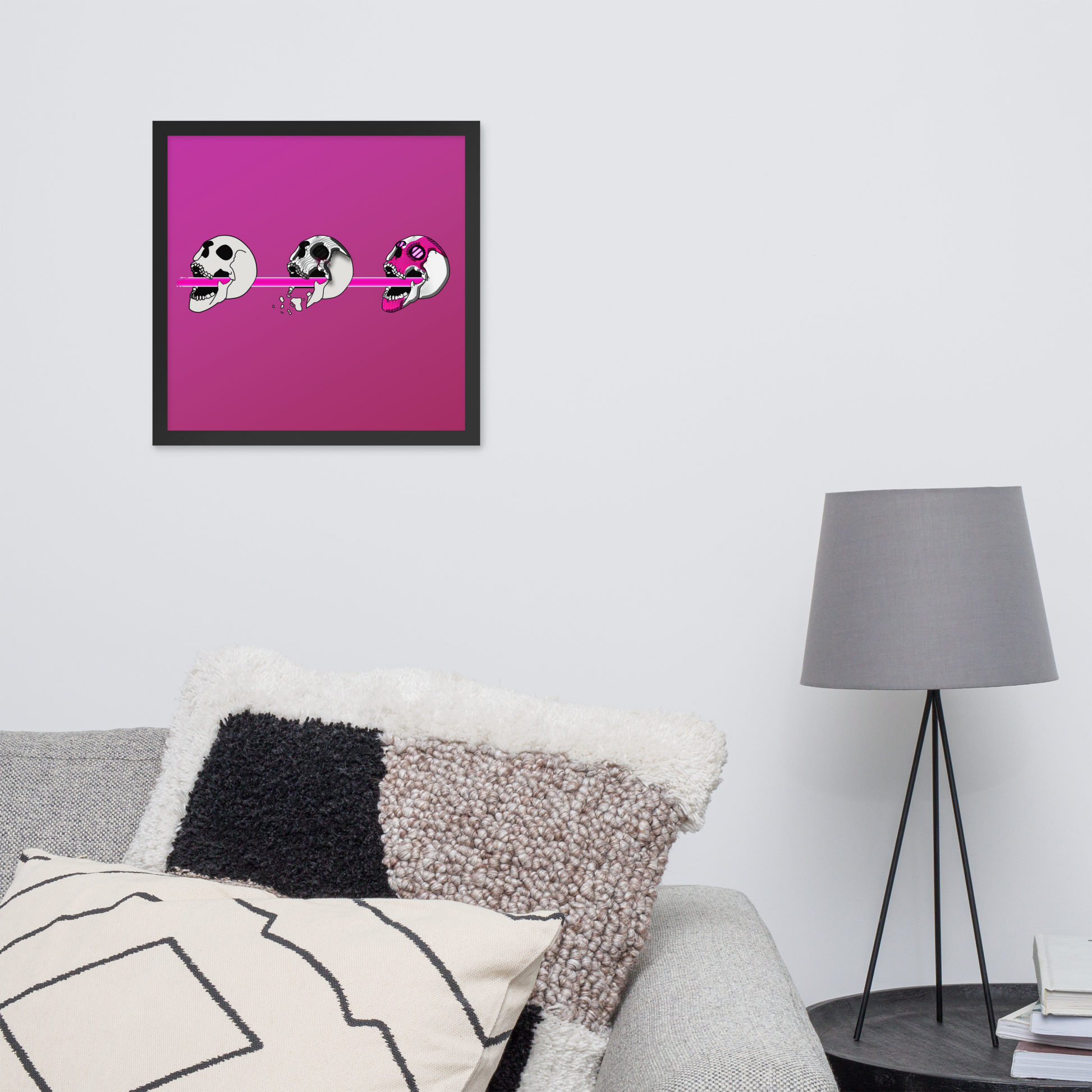 Framed 16x16 artwork of a pink background and three stylized cyberpunk skull designs shooting a laser with purple and black details in a living room setting.