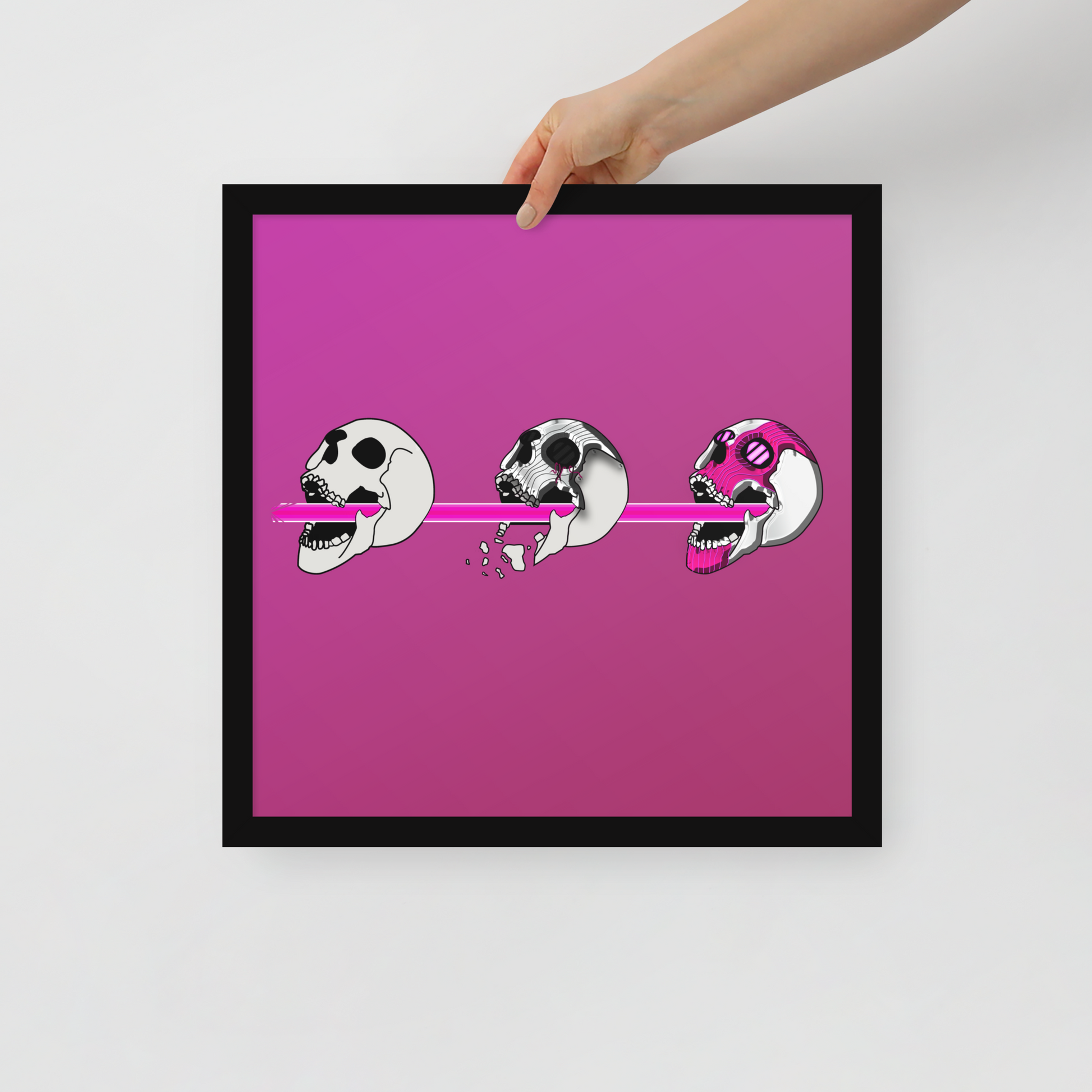 Framed artwork with a pink background and black frame, featuring three stylized skulls.