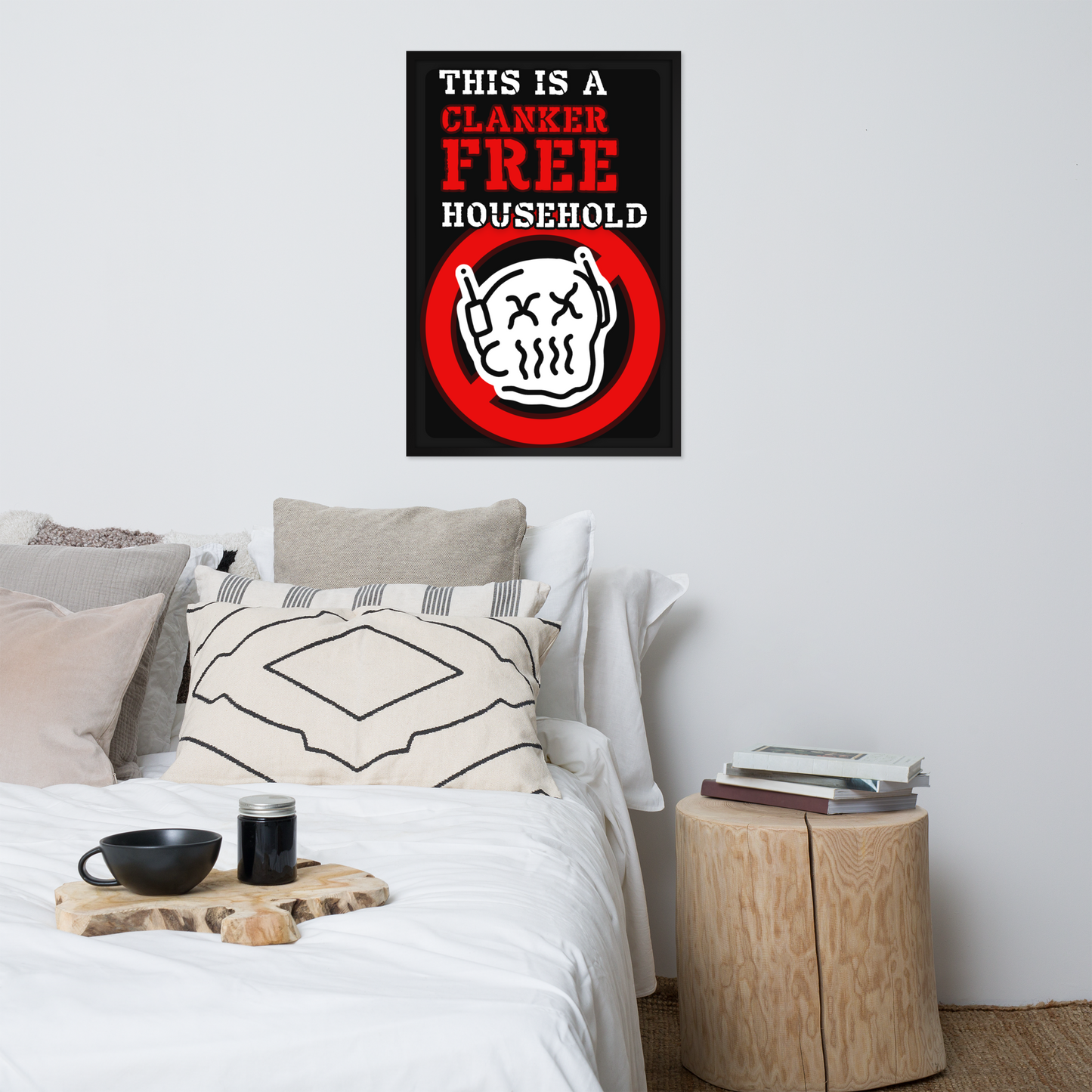 A bedroom scene with a bed, pillows, side table, and a framed wall poster above the bed. The poster has a black background with red and white text reading 'THIS IS A CLANKER FREE HOUSEHOLD' and a cartoon skull-and-crossbones inside a red circle.