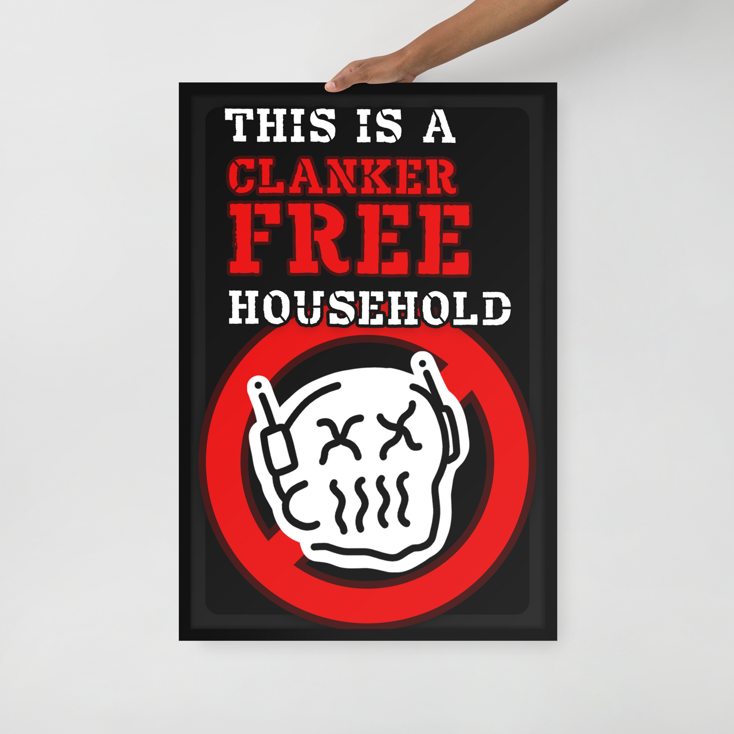 A rectangular novelty sign with a black background and bold text reading 'THIS IS A CLANKER FREE HOUSEHOLD' in white and red, plus a red prohibition symbol over a cartoon clanker face. A hand is holding the top edge of the sign against a light gray wall.