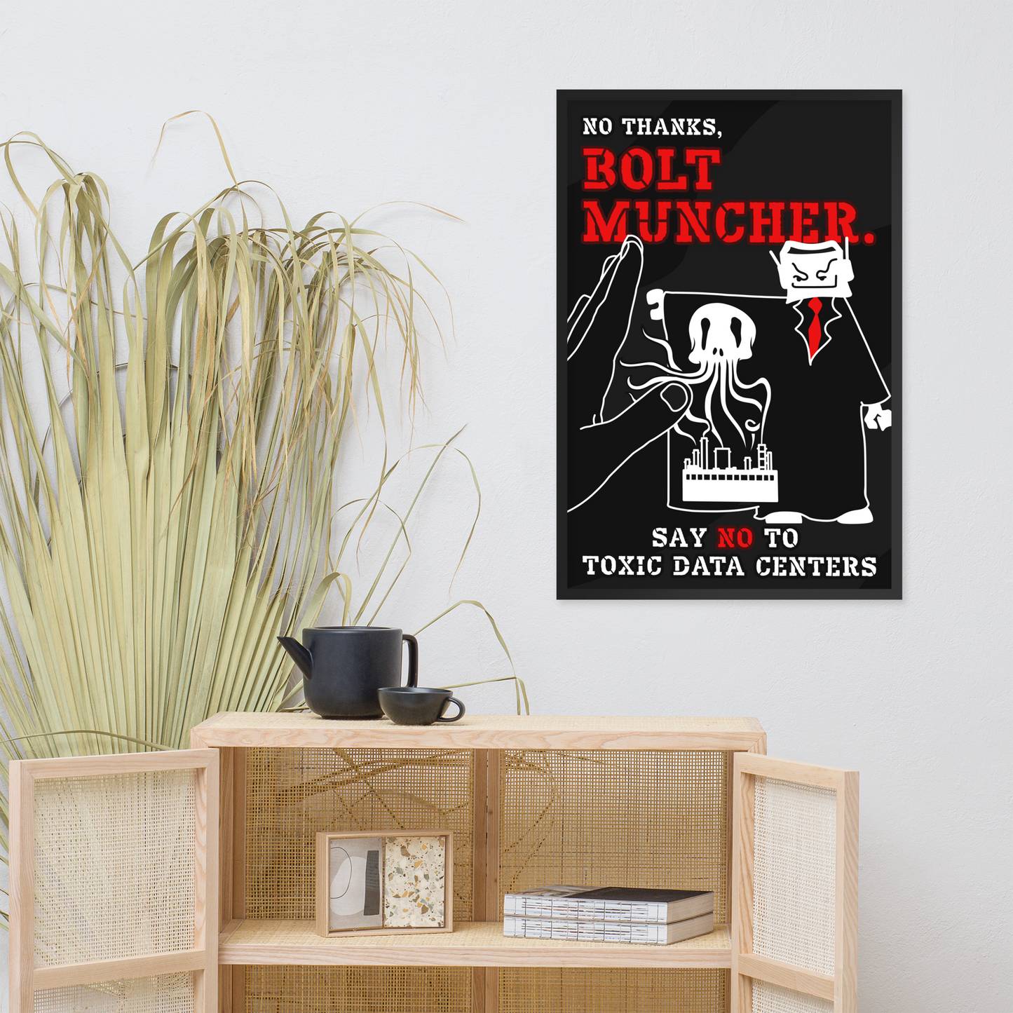 A framed black poster with red and white text reading 'NO THANKS, BOLT MUNCHER.' and 'SAY NO TO TOXIC DATA CENTERS' hangs on a light gray wall above a wooden cabinet.
