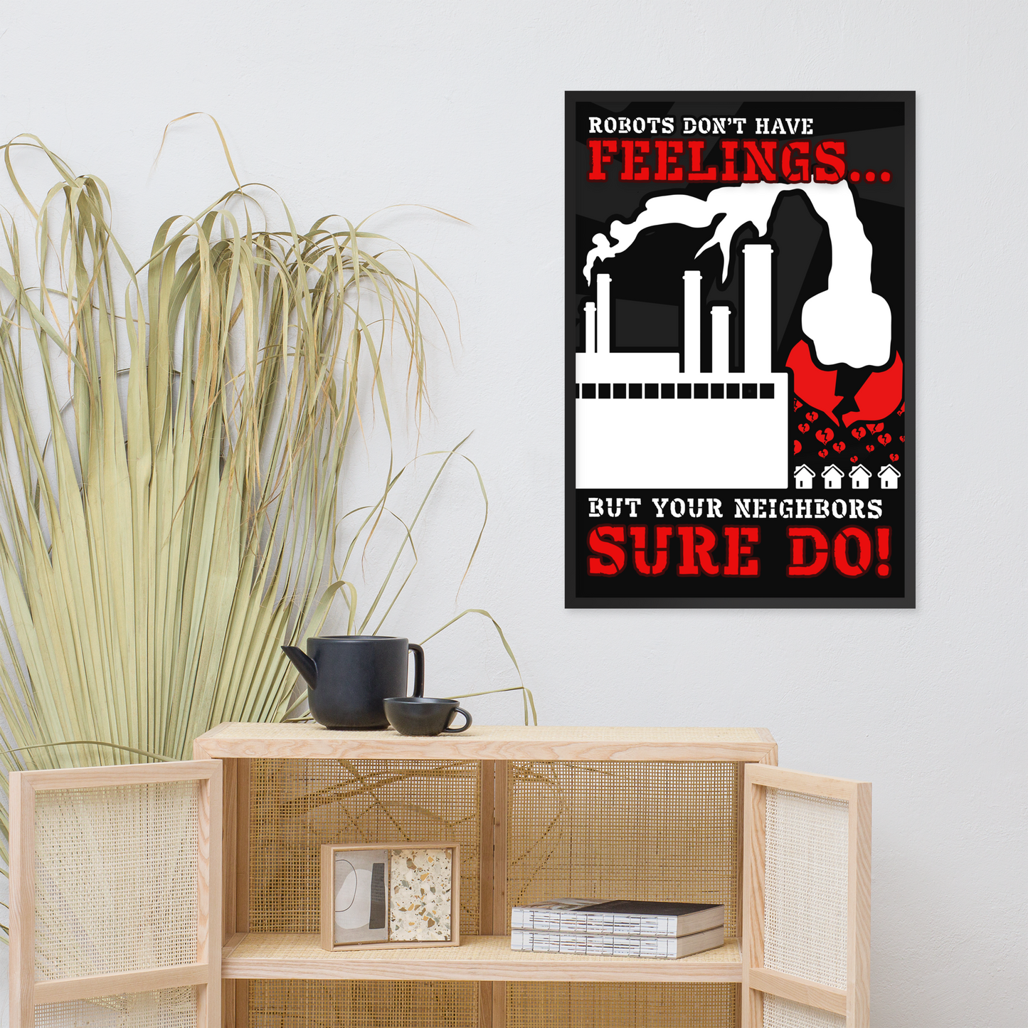 A framed wall poster with a humorous quote and graphic illustration hanging on a light gray wall above a wooden cabinet with a black teapot and books.