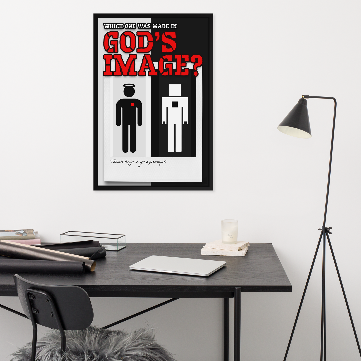 A framed minimalist art print titled 'God's Image?' hangs on a white wall above a dark desk in a modern office setting. The print features a black and white background with bold red title text and two simple human figures, one with a red cross on the chest.