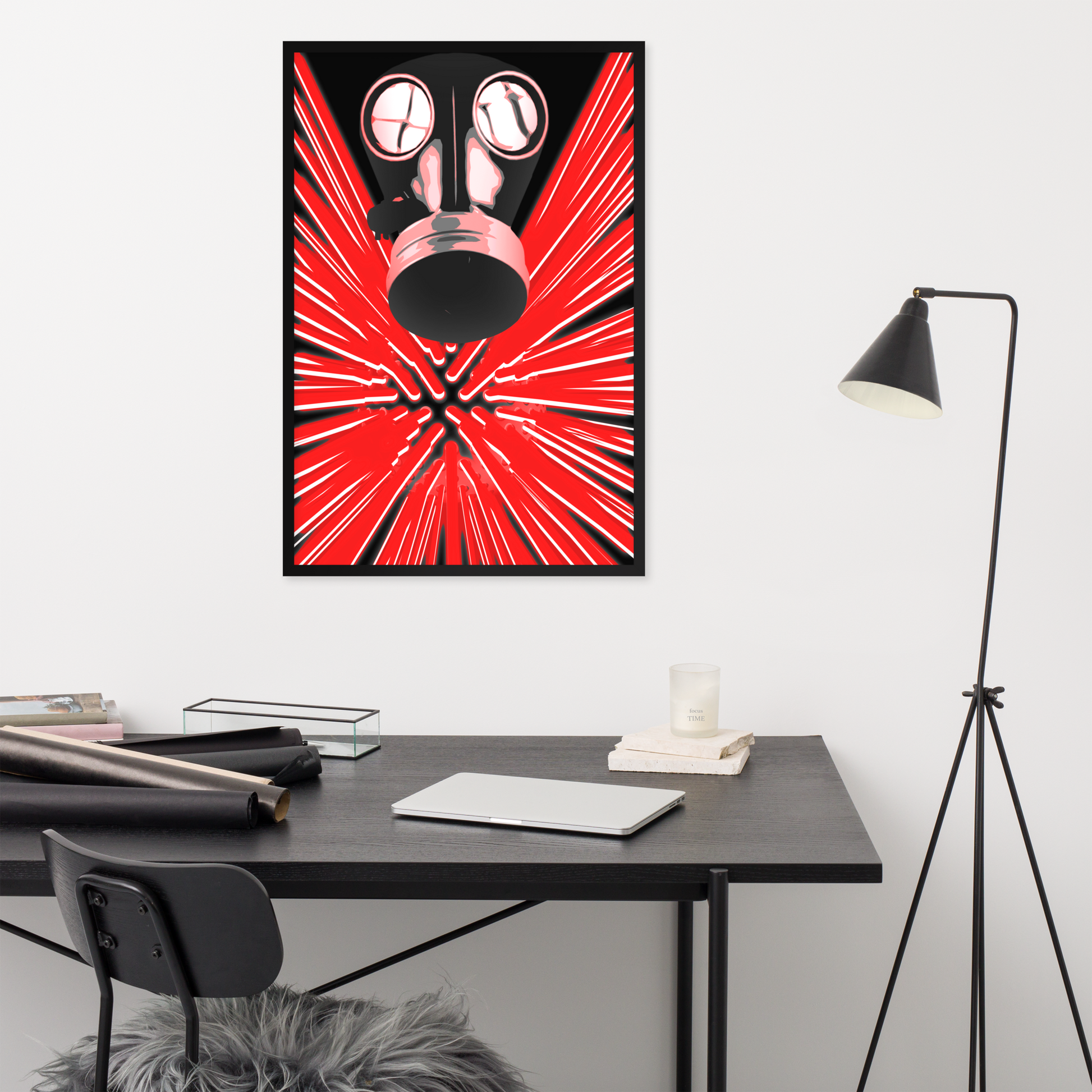 A framed wall art print featuring a stylized red and black gas mask with radiating light streaks, displayed above a dark desk in a modern room with a floor lamp, chair, and small decor items.